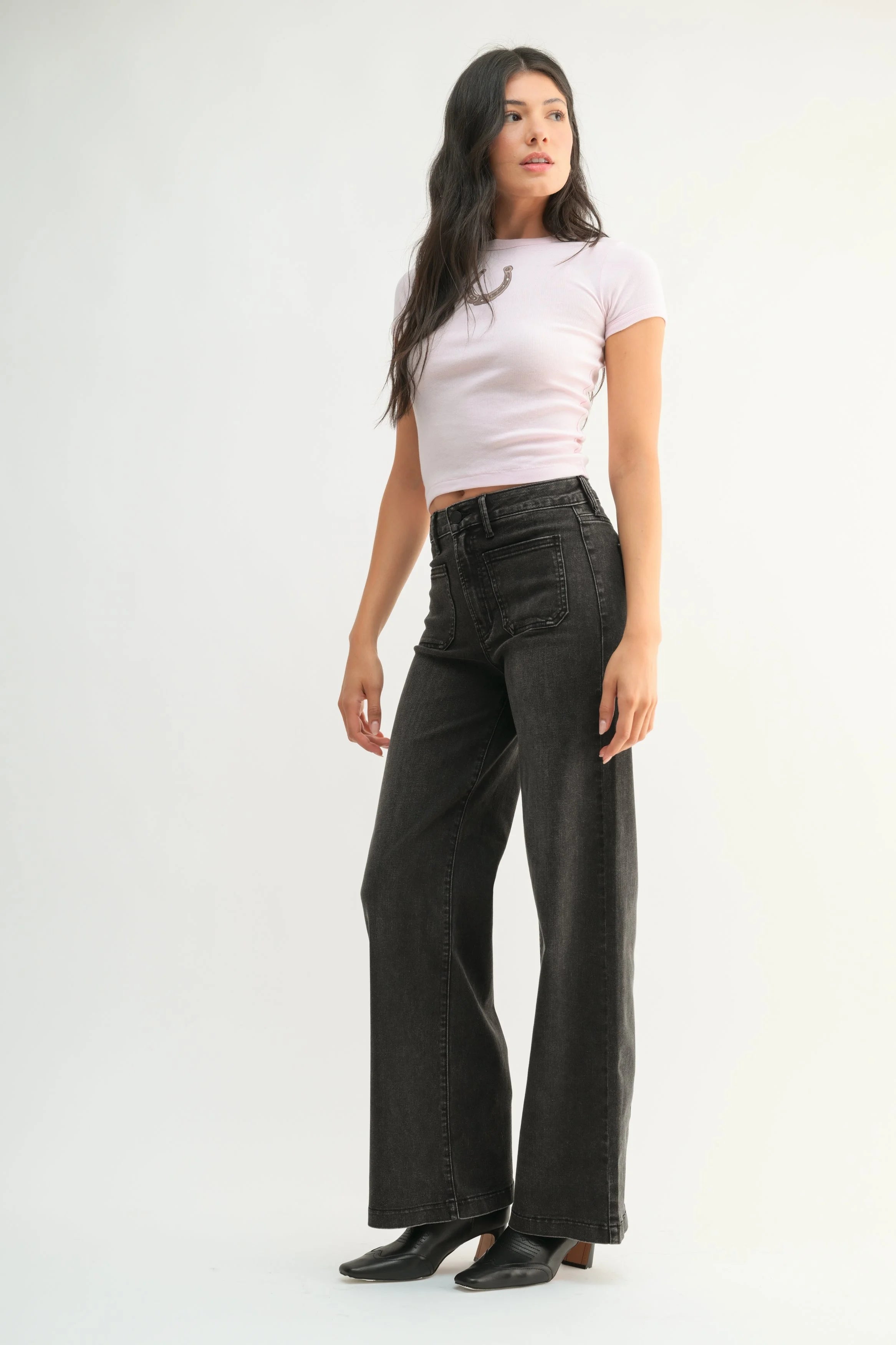 Woman wearing black wide-leg jeans and a light pink top on a white background