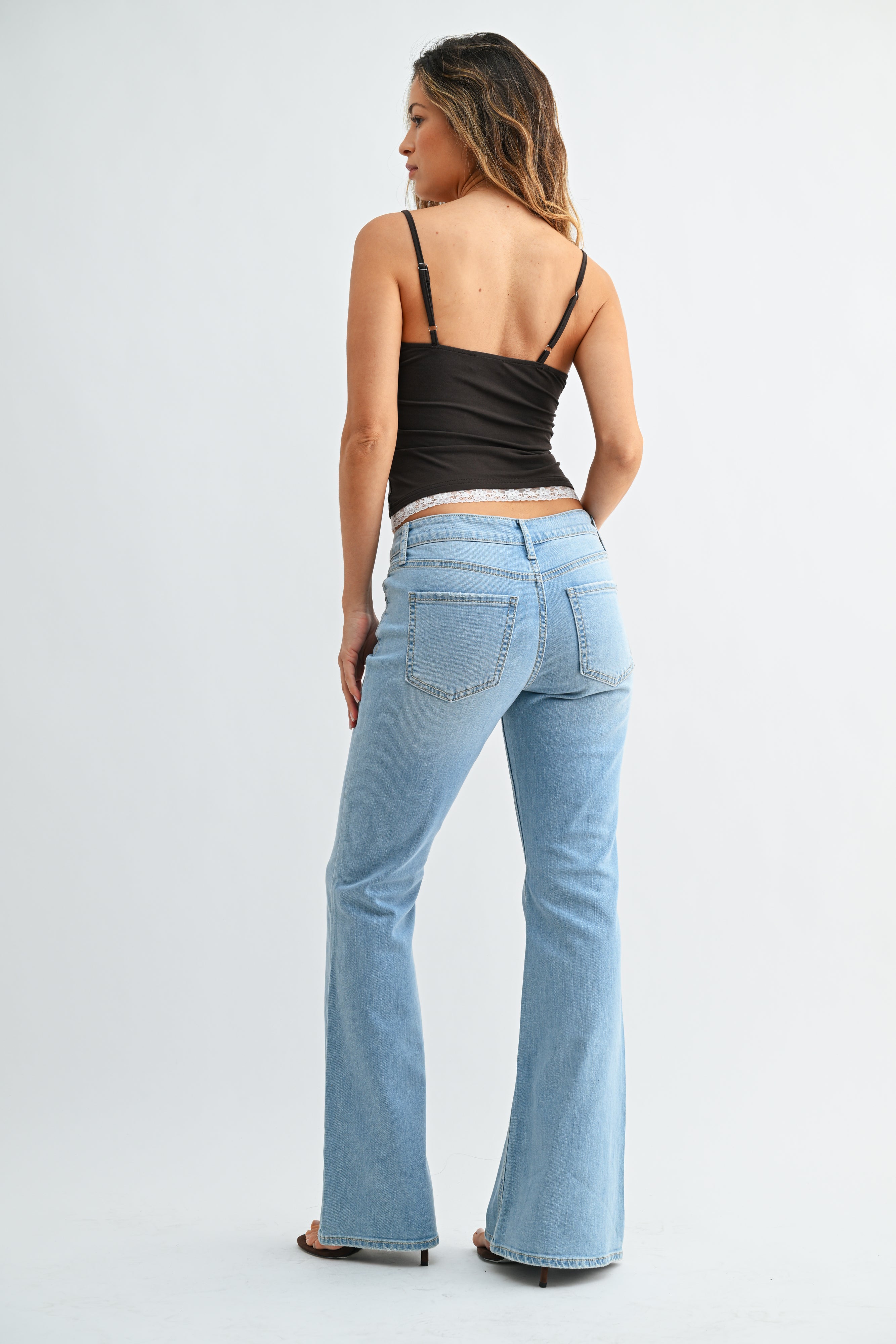 Woman wearing light blue flared jeans and a black top on a white background