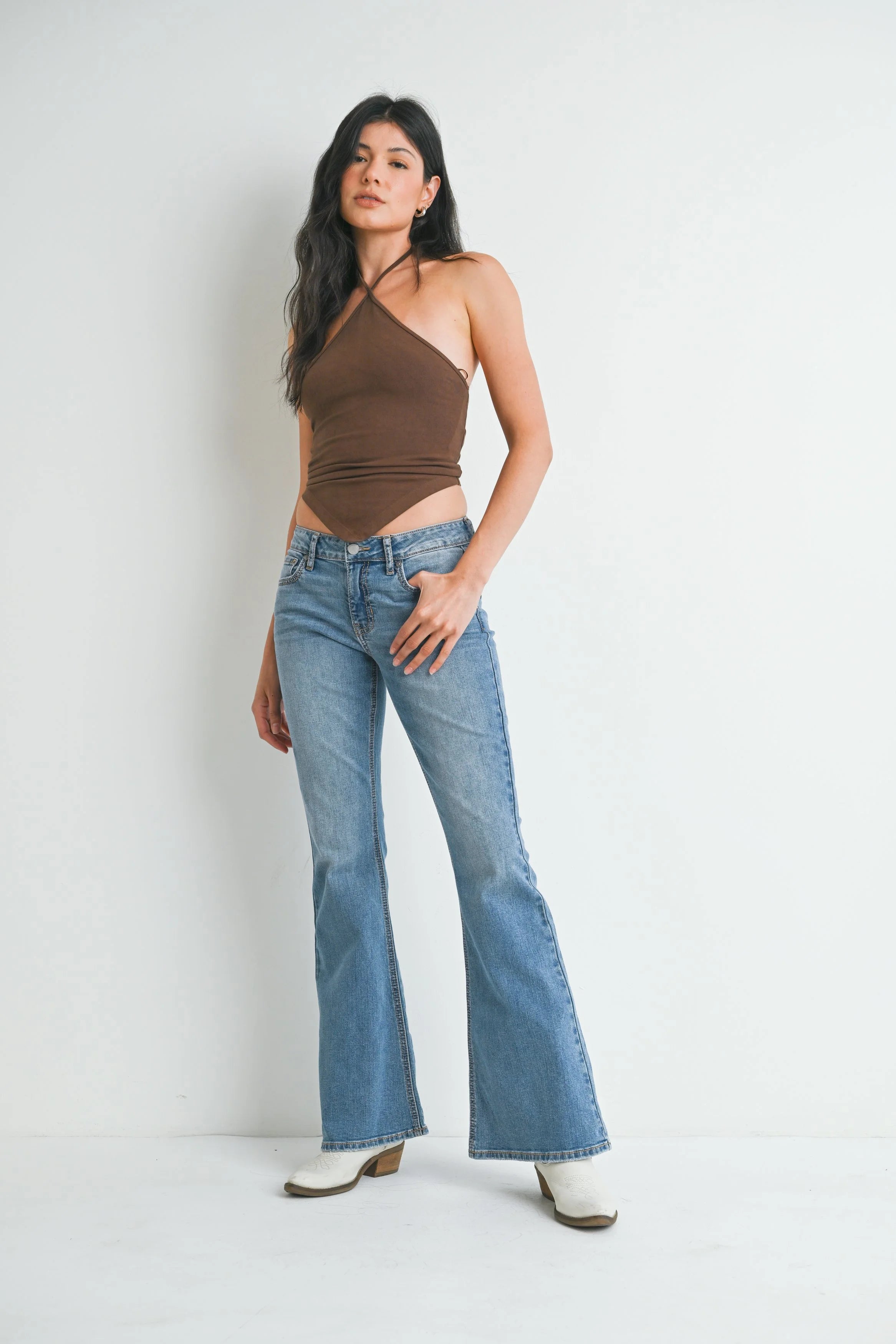 Woman wearing a brown halter top and blue flared jeans on a white background