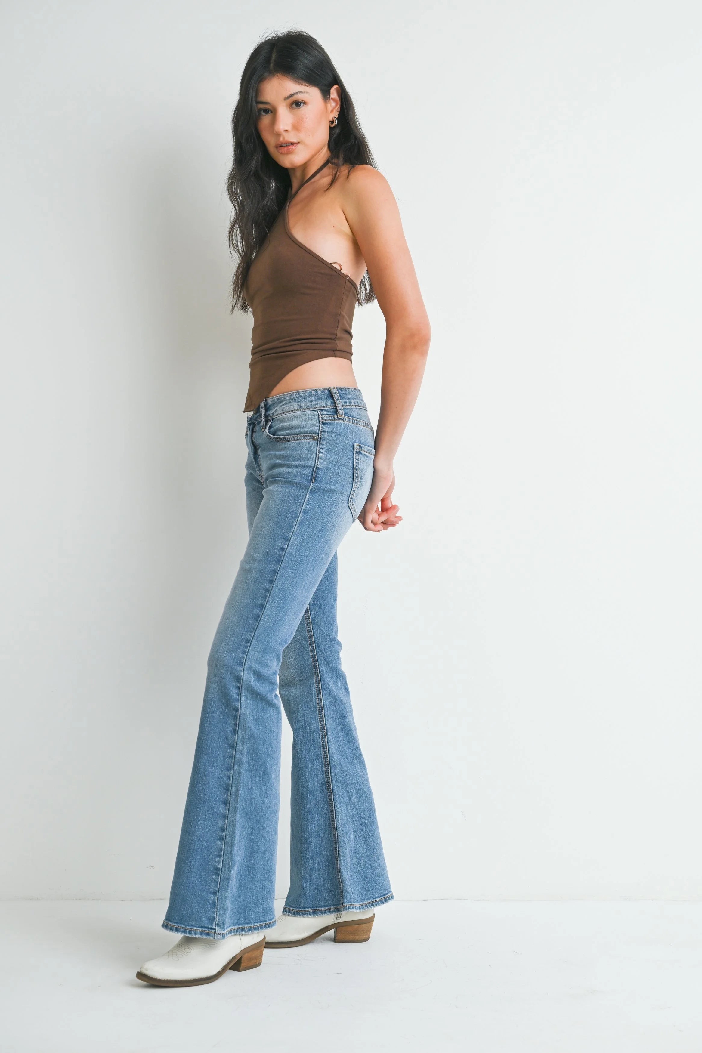 Woman wearing a brown top and blue flared jeans against a white background