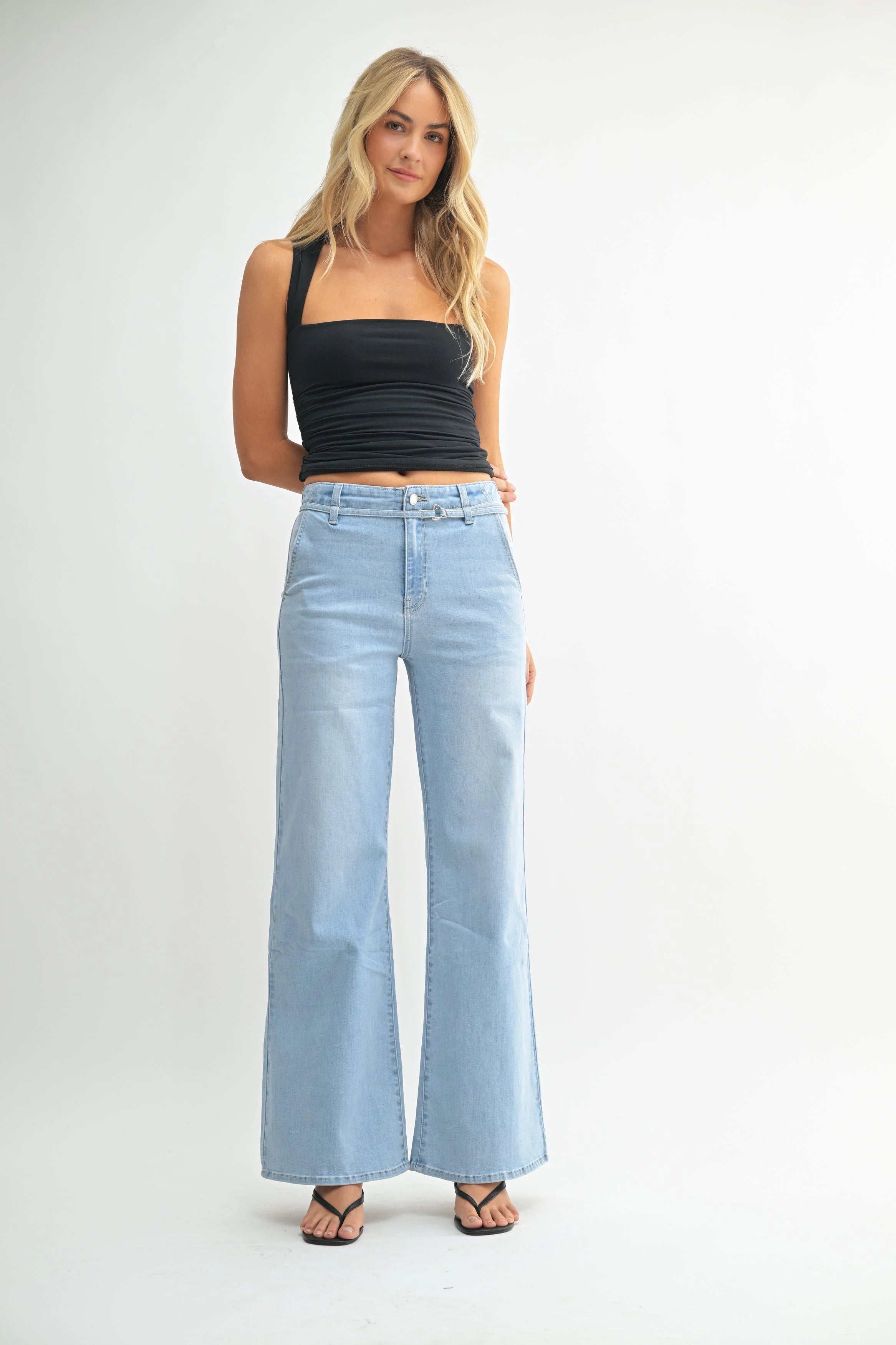 Woman wearing light blue jeans and a black top on a white background