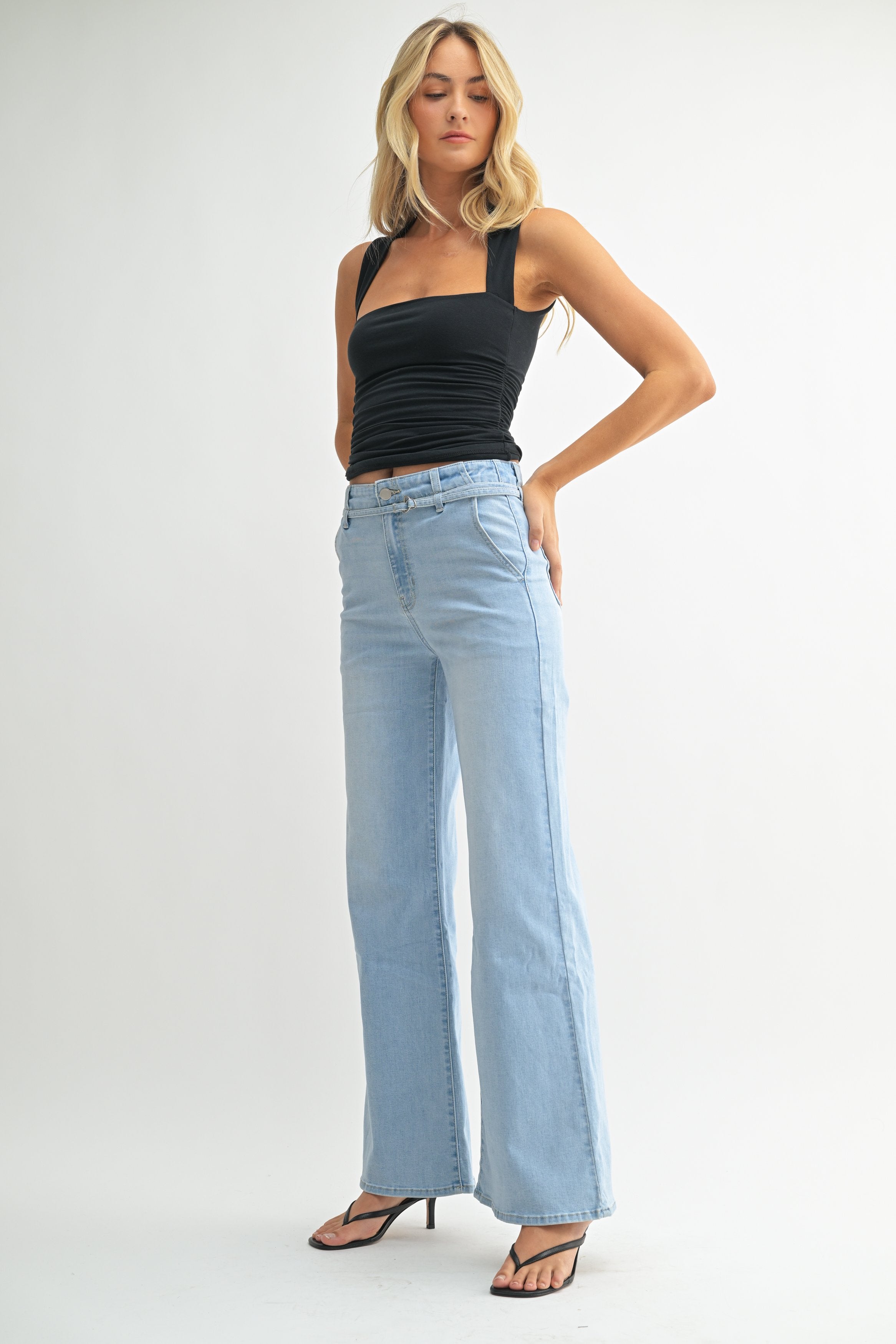 Woman wearing light blue jeans and a black top on a white background