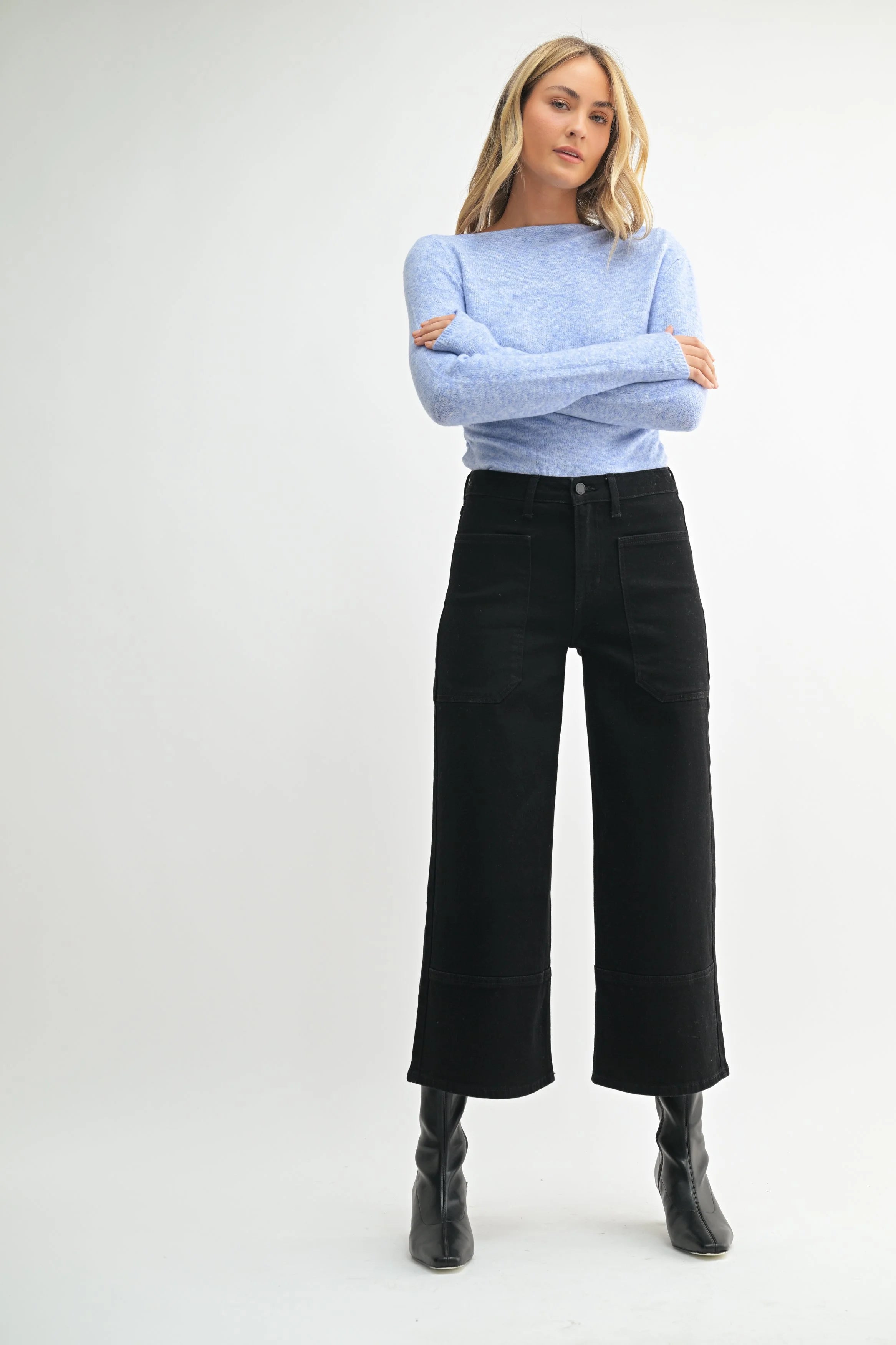 Woman wearing a light blue sweater and black pants on a white background