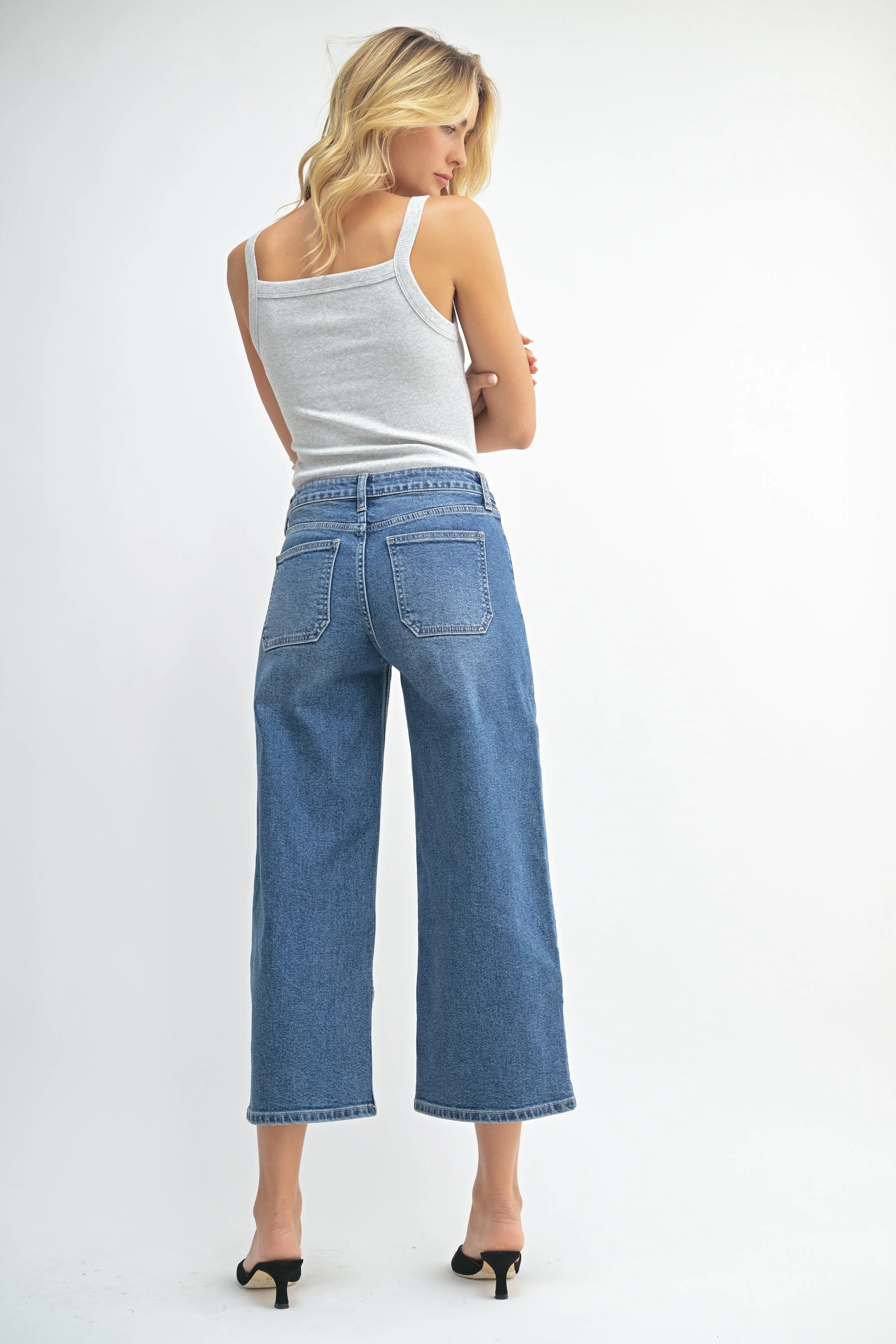 Woman wearing blue jeans and a white tank top on a white background