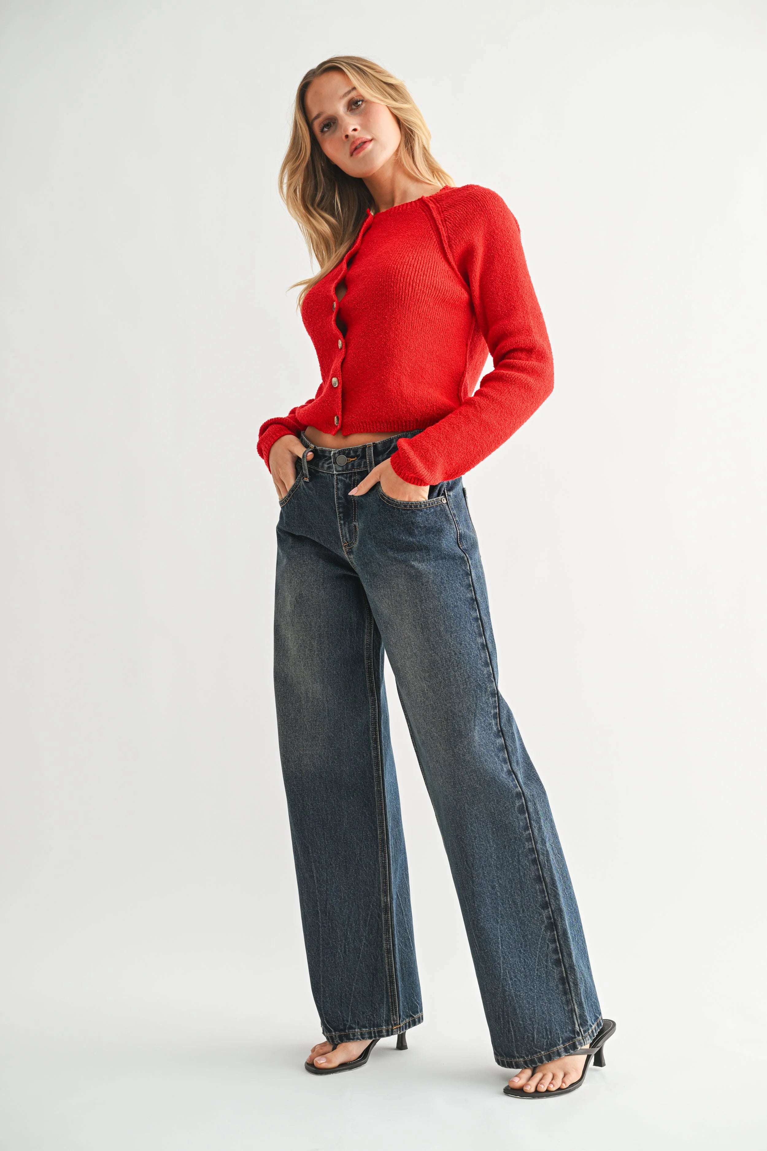 Woman wearing a red cardigan and blue jeans on a white background