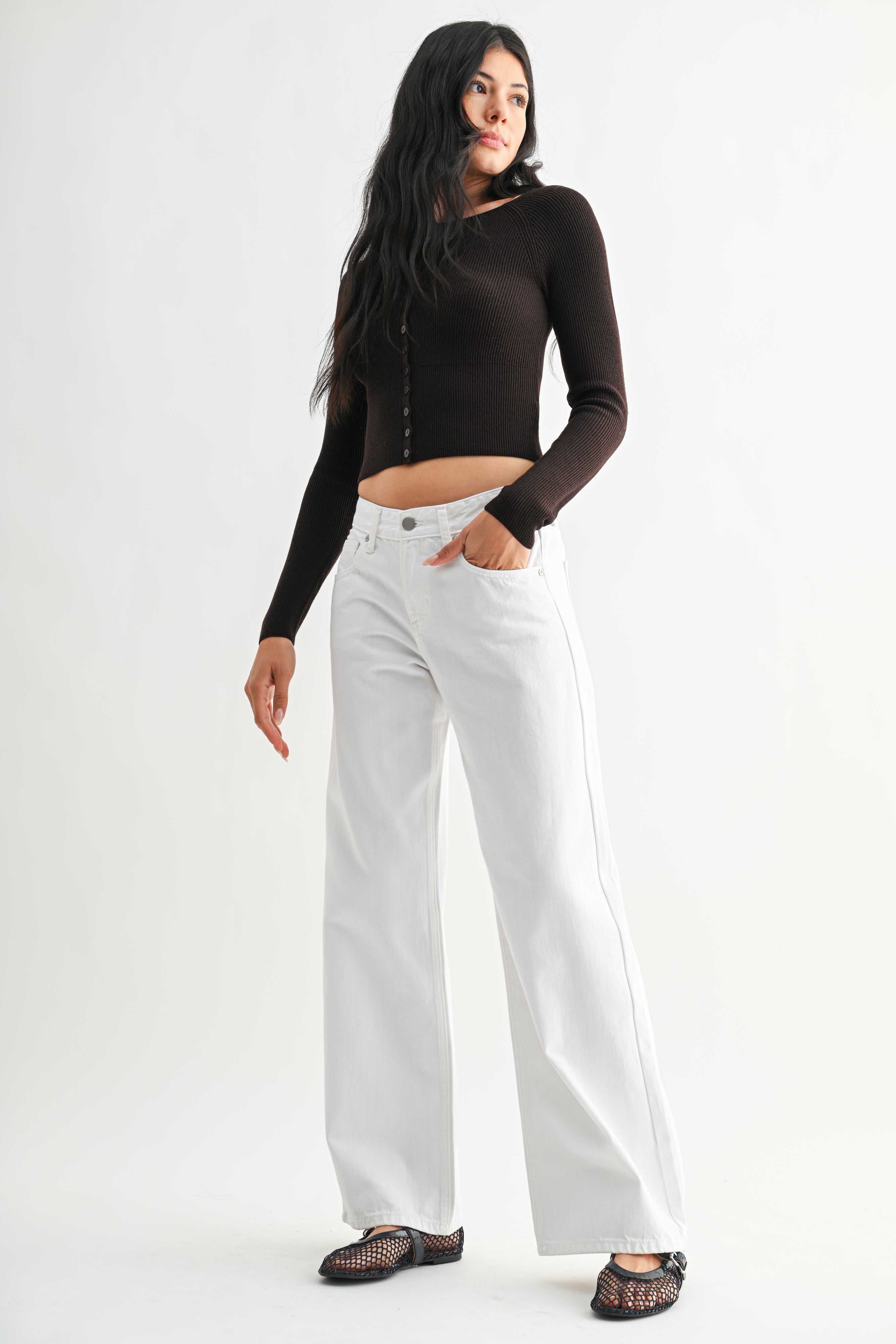 Woman wearing a black long-sleeve top and white pants on a white background