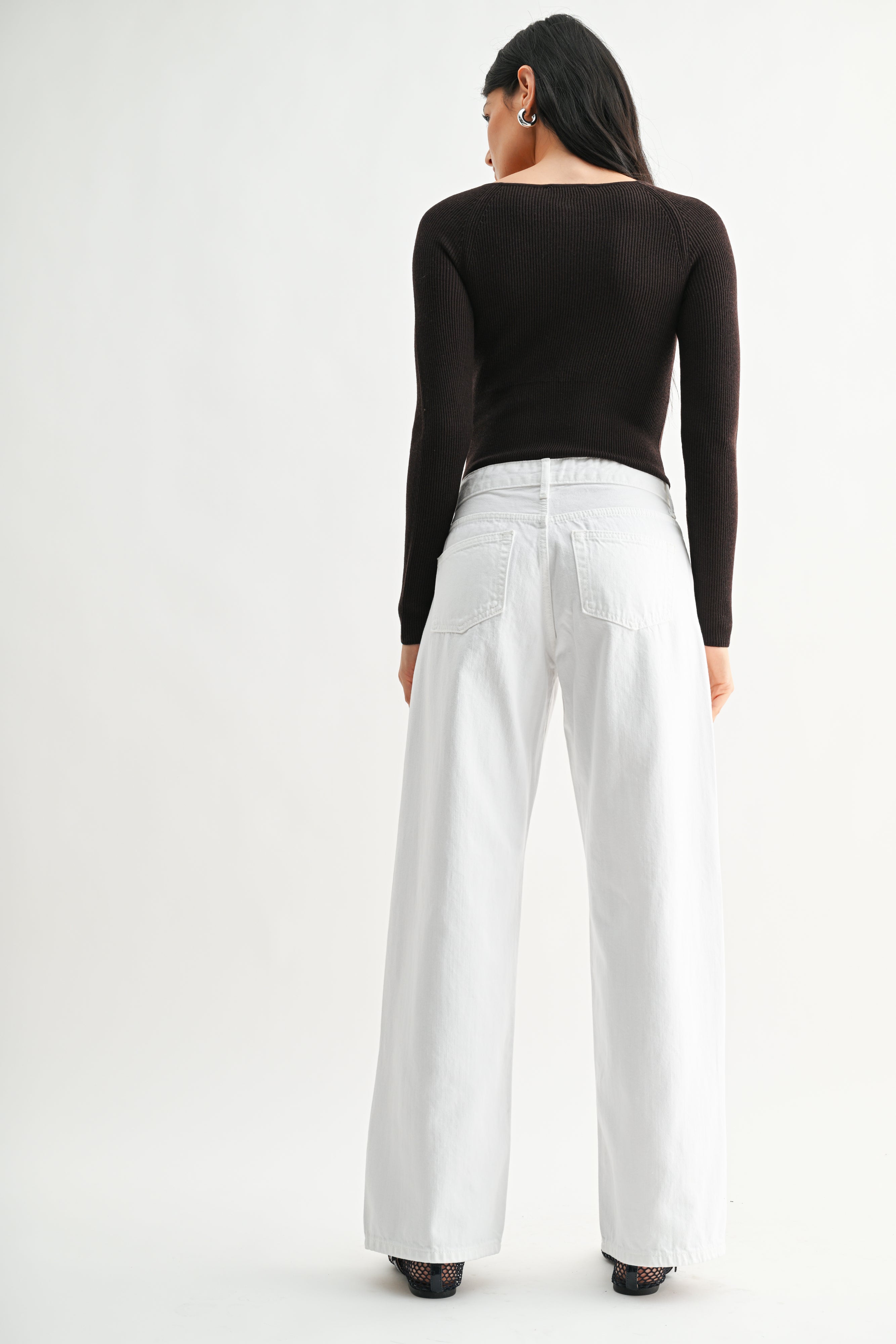 Woman wearing a black top and white pants on a white background