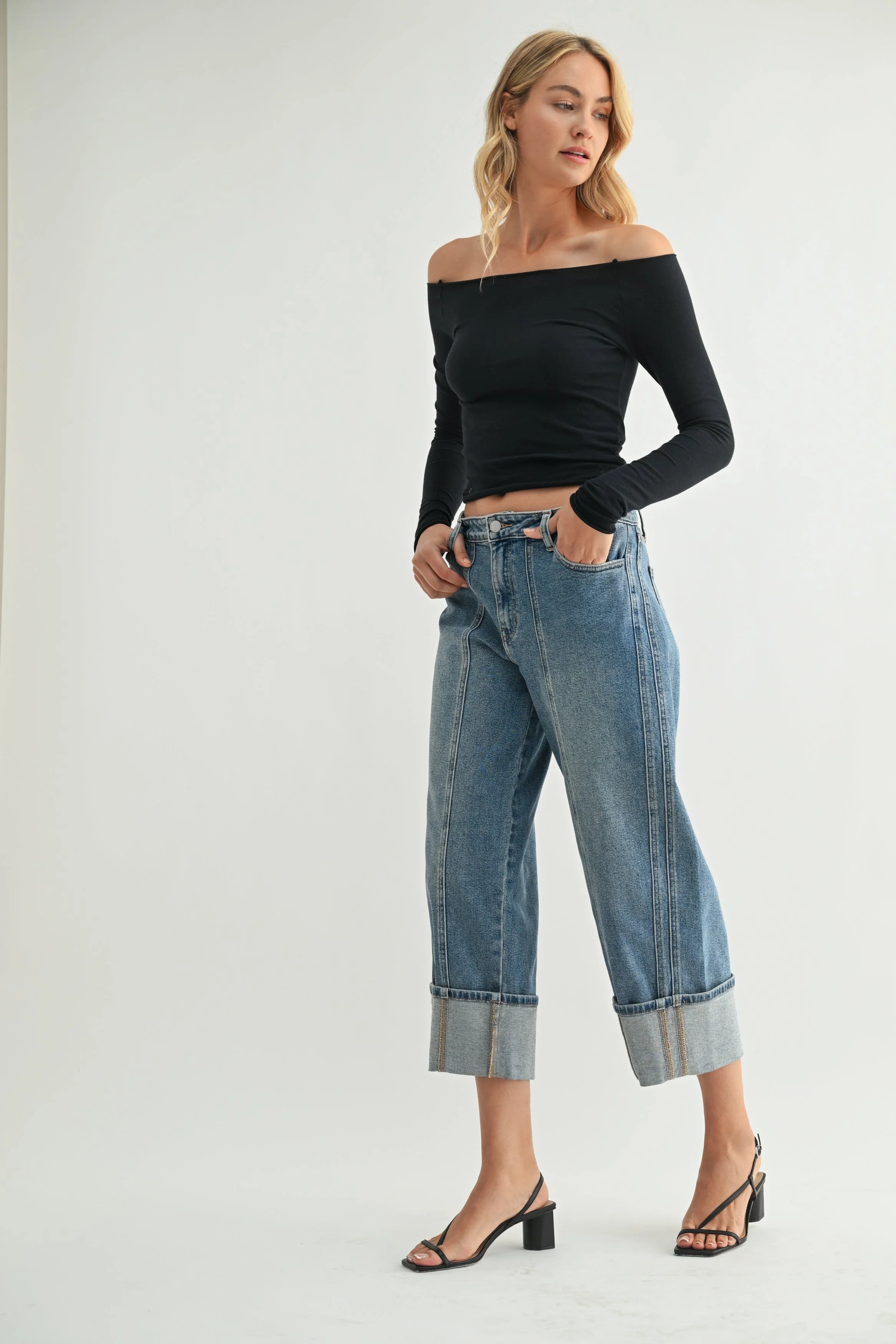 Woman wearing a black off-shoulder top and blue jeans on a white background