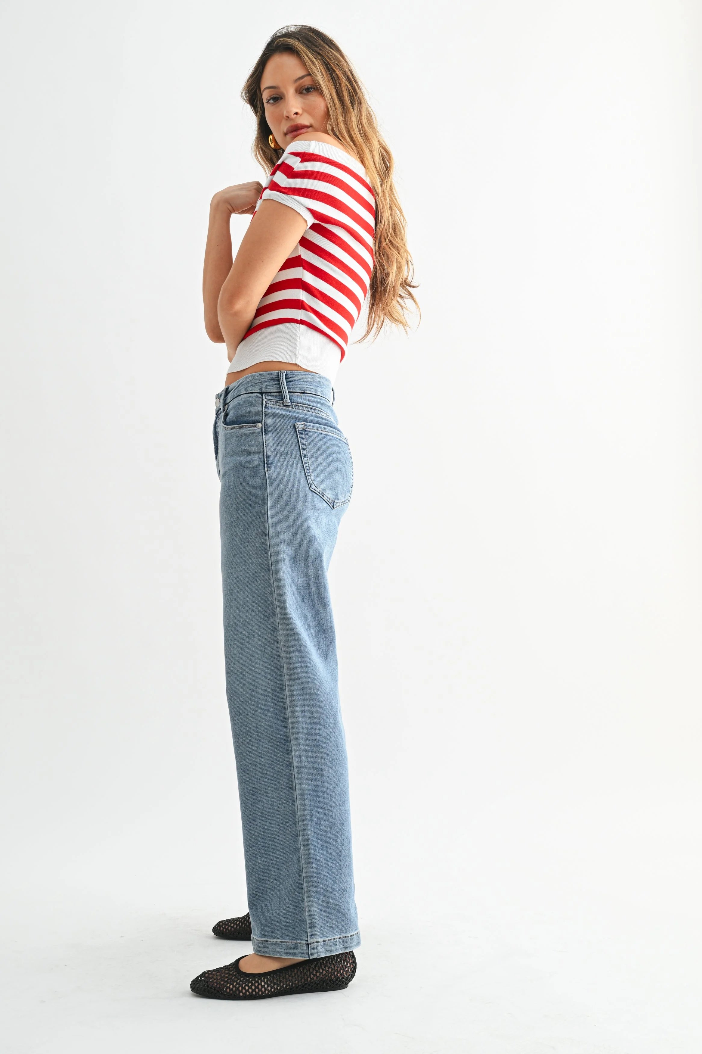 Woman wearing a red and white striped crop top and light blue jeans on a white background