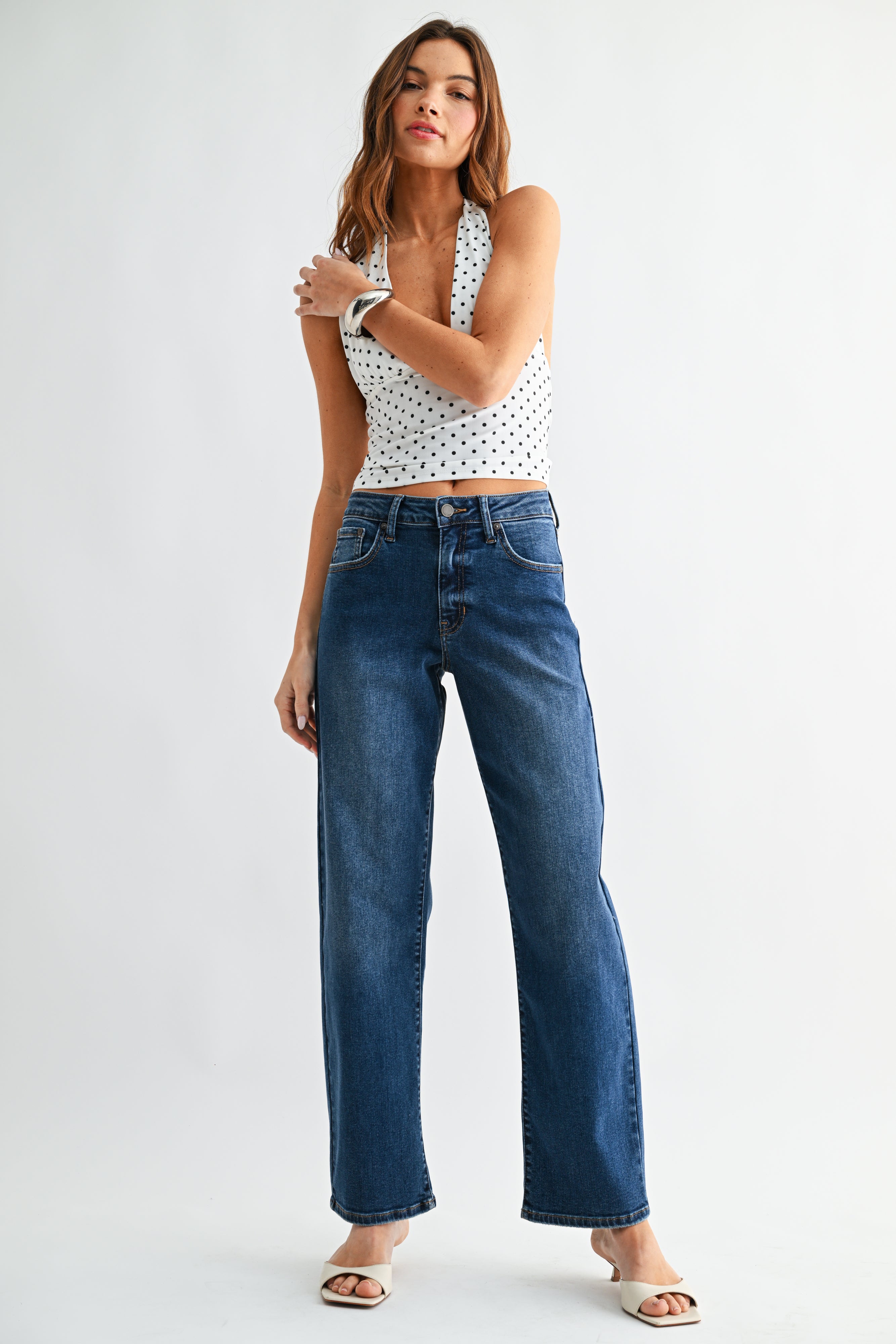 Woman wearing a polka dot top and blue jeans on a white background