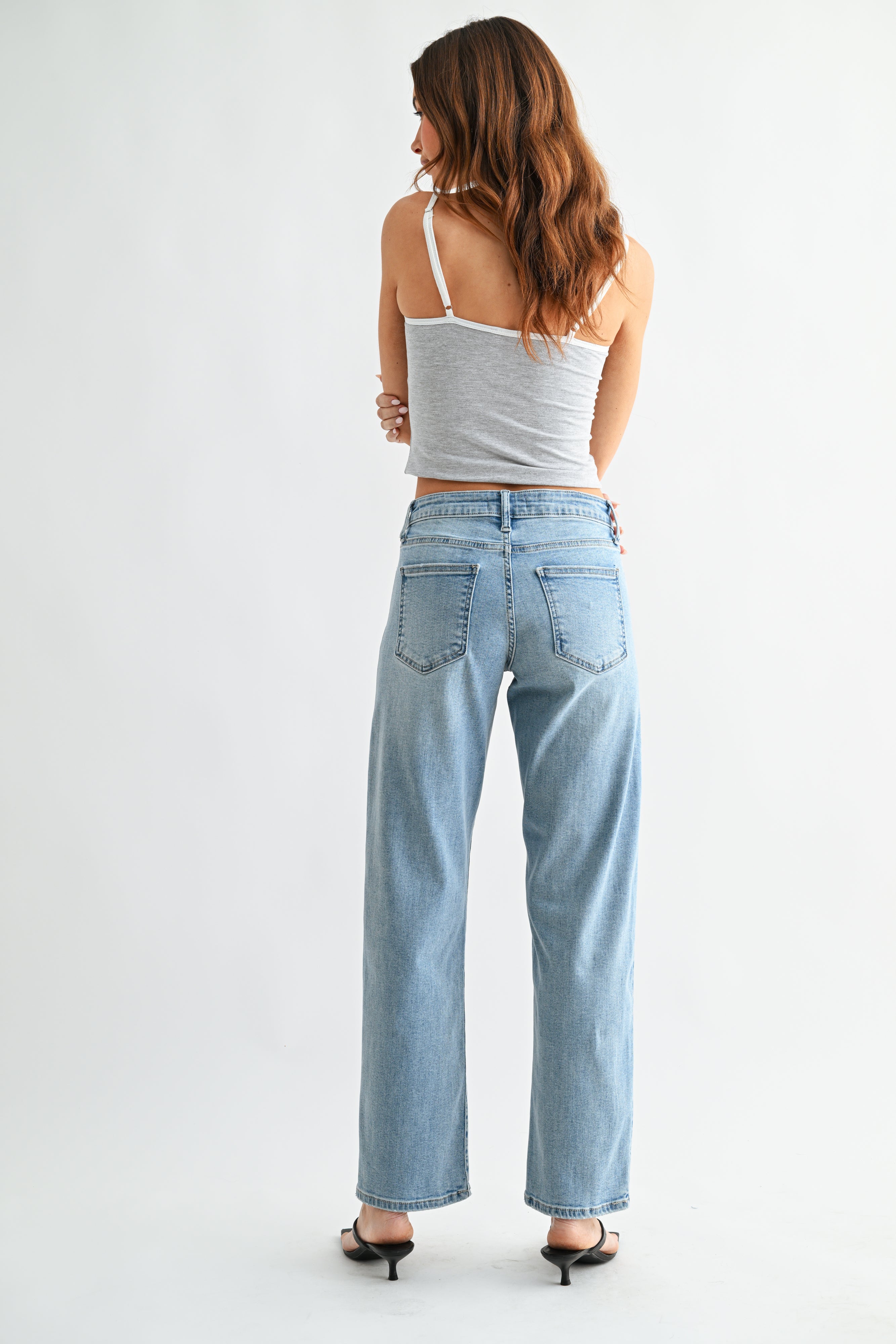 Woman wearing light blue jeans and a white top on a white background