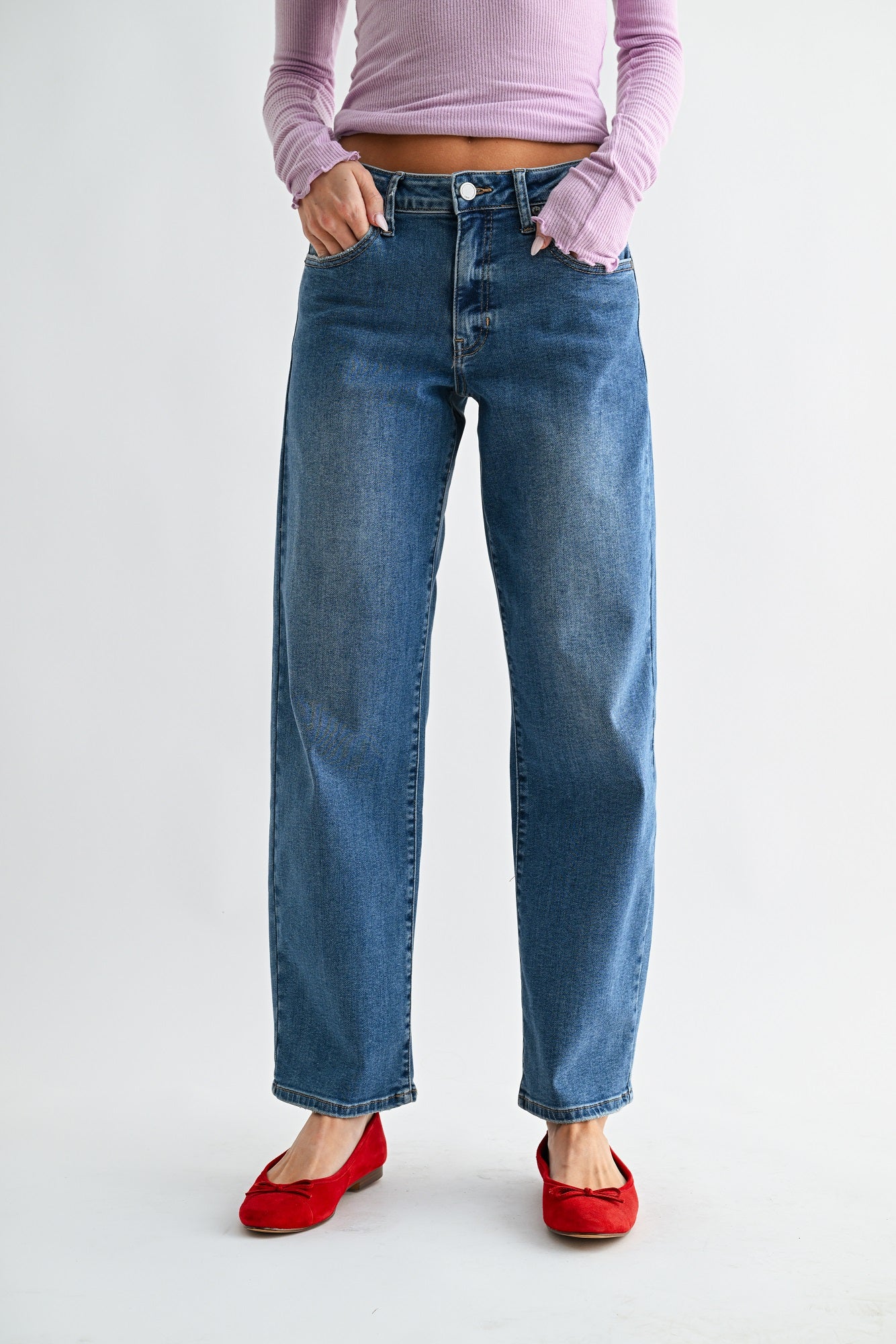 Person wearing blue jeans and a pink top on a light gray background