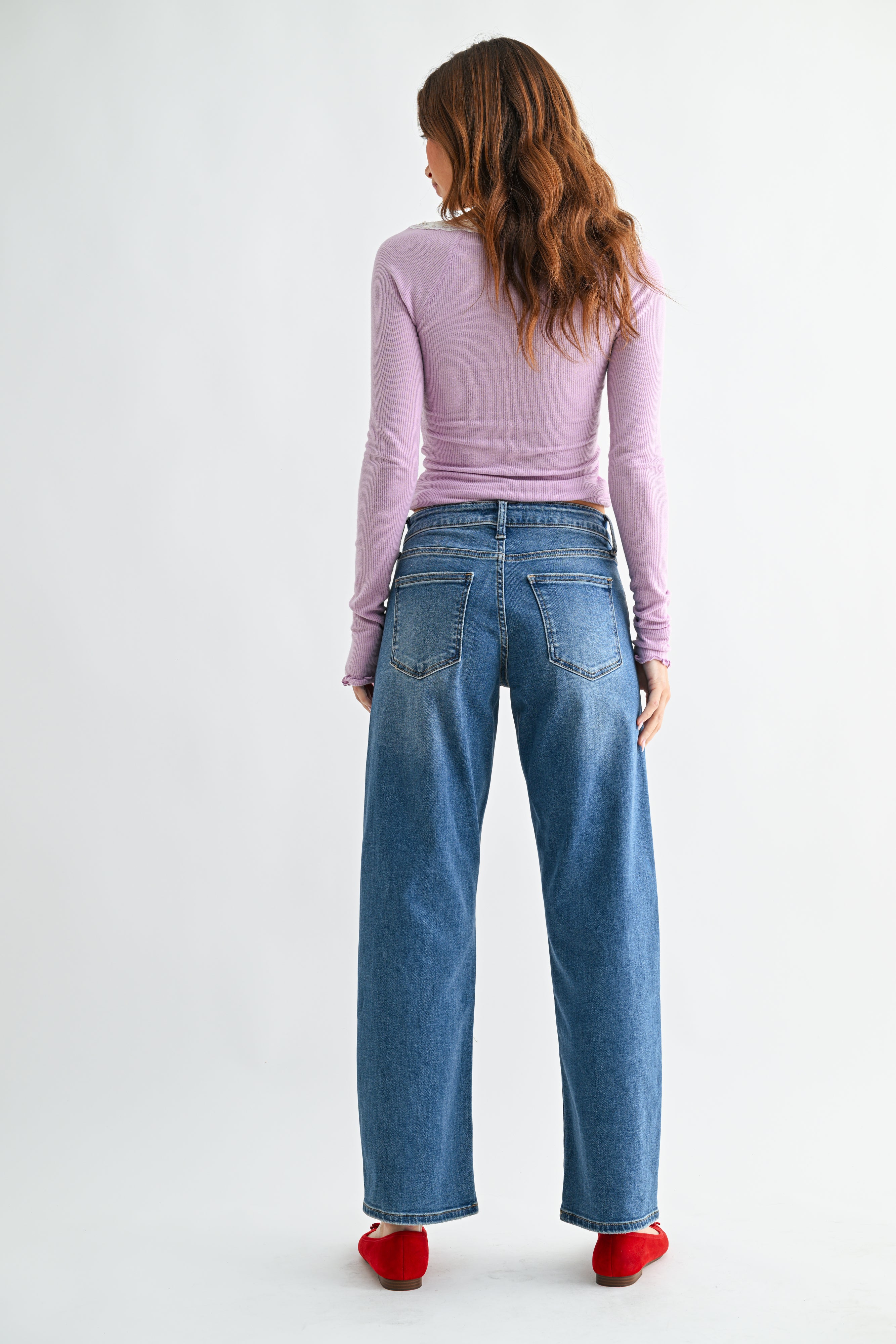 Woman wearing blue jeans and a light purple top on a white background