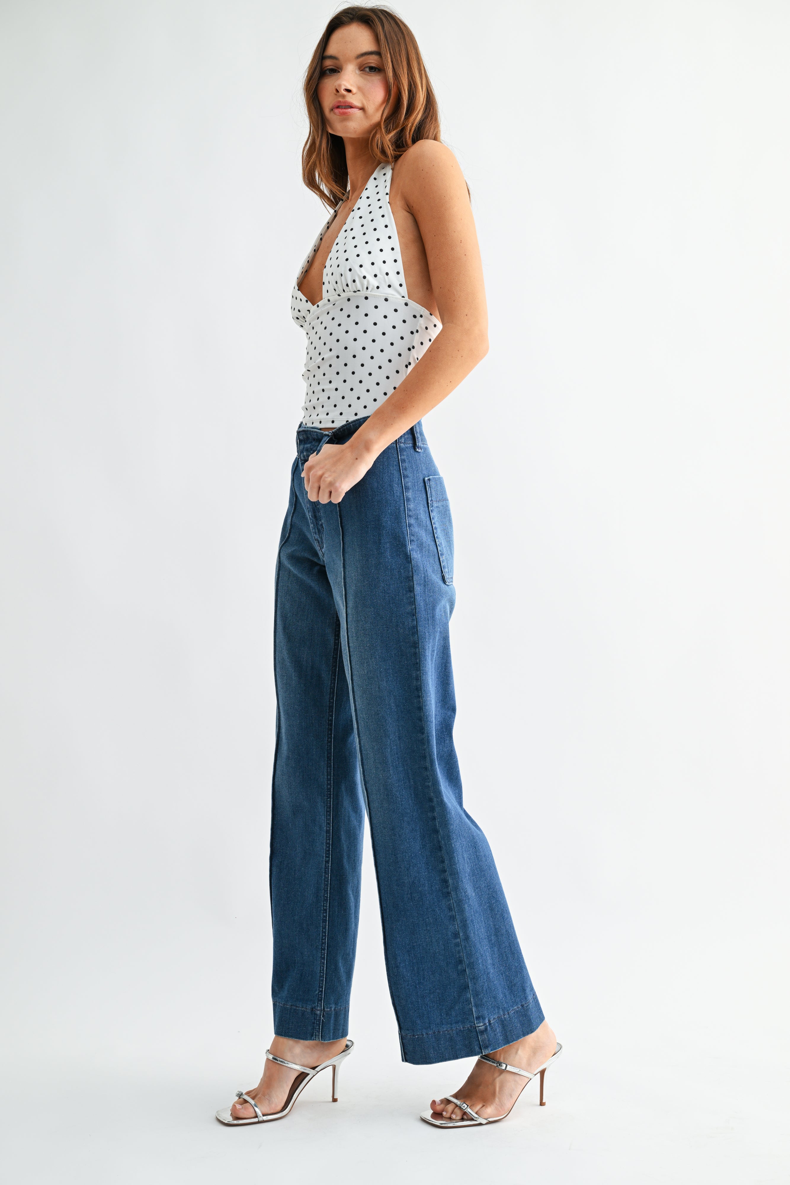 Woman wearing a polka dot top and blue jeans on a white background