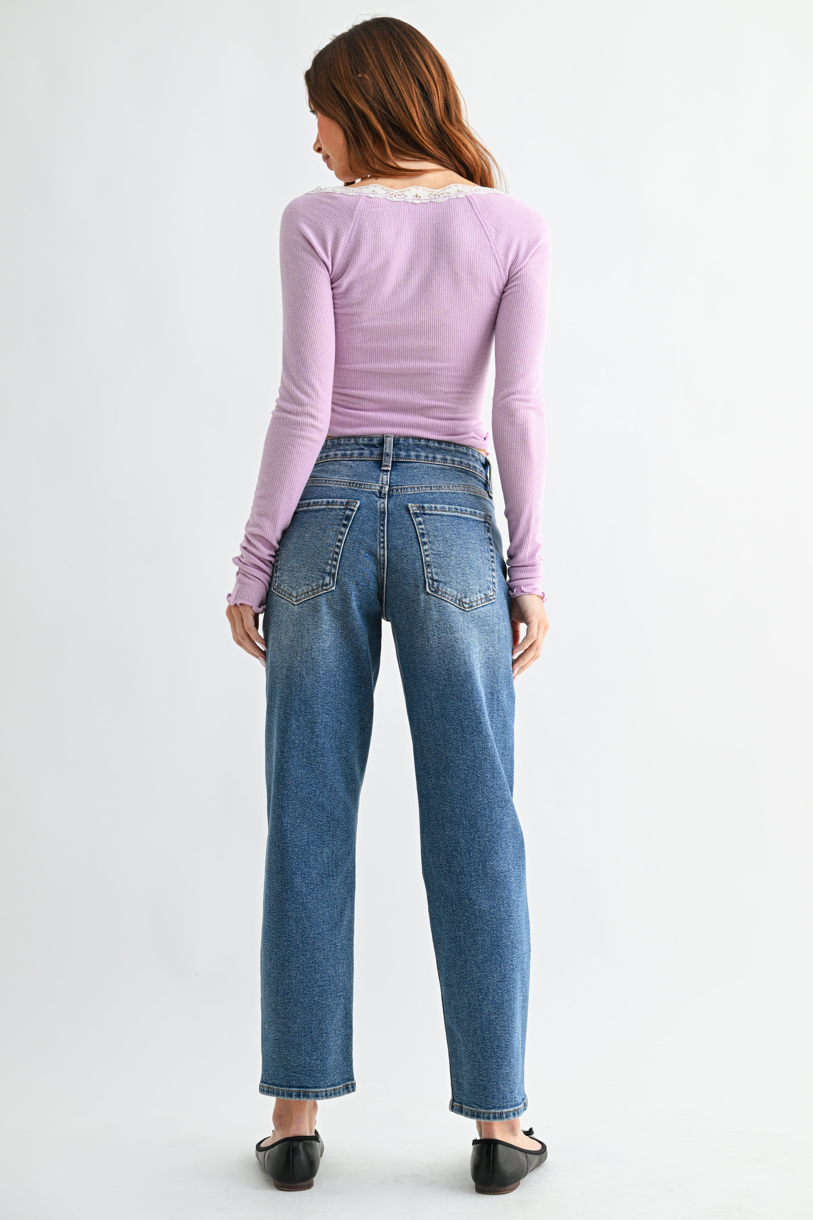Person wearing a light purple long-sleeve top and blue jeans on a white background