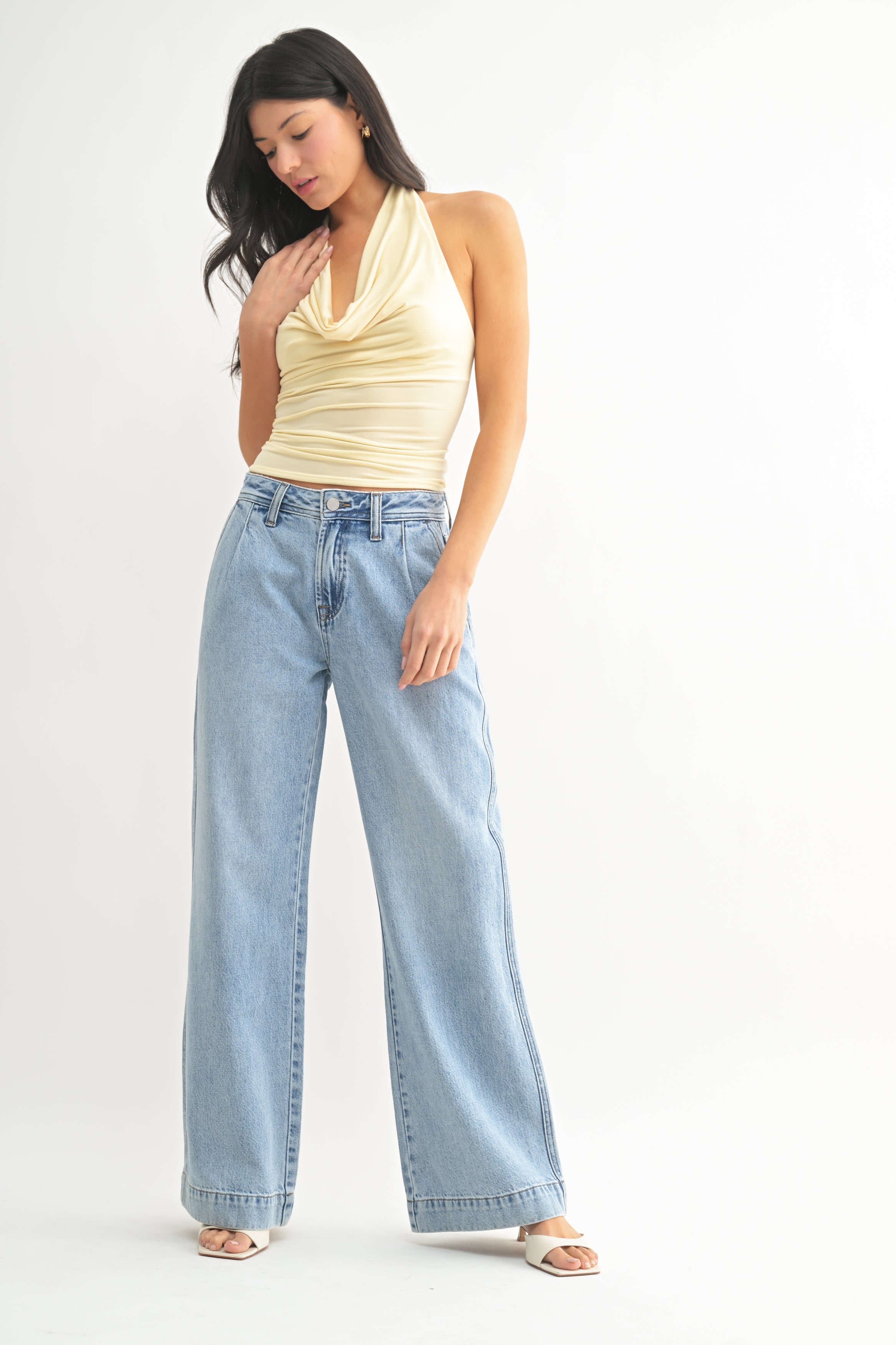 Woman wearing a yellow top and light blue jeans on a white background