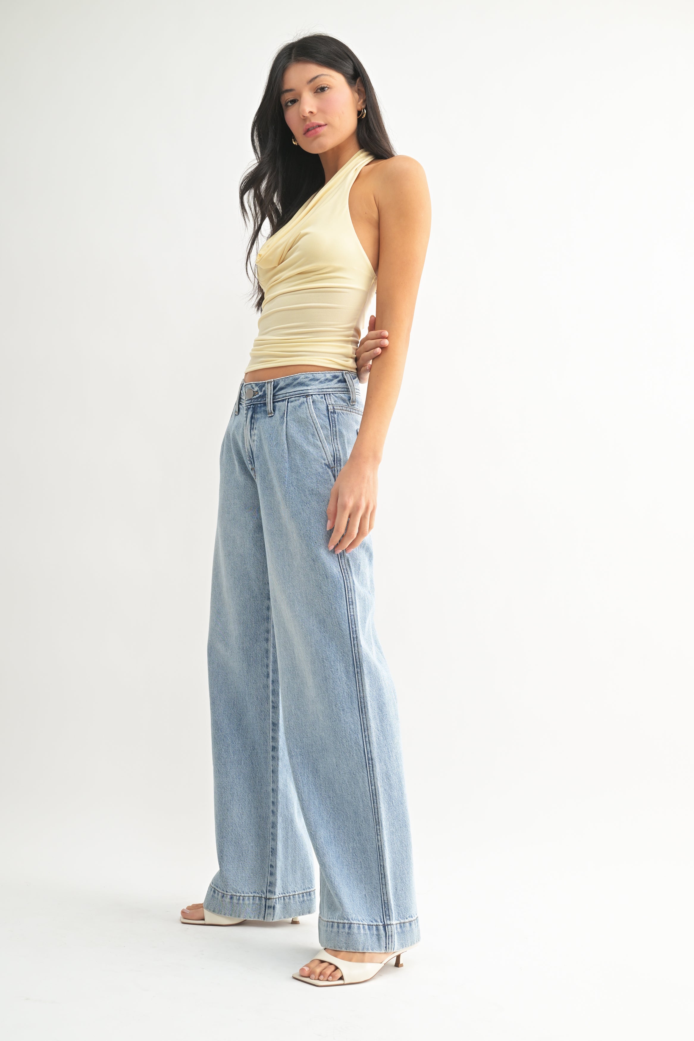 Woman wearing a yellow top and light blue jeans on a white background