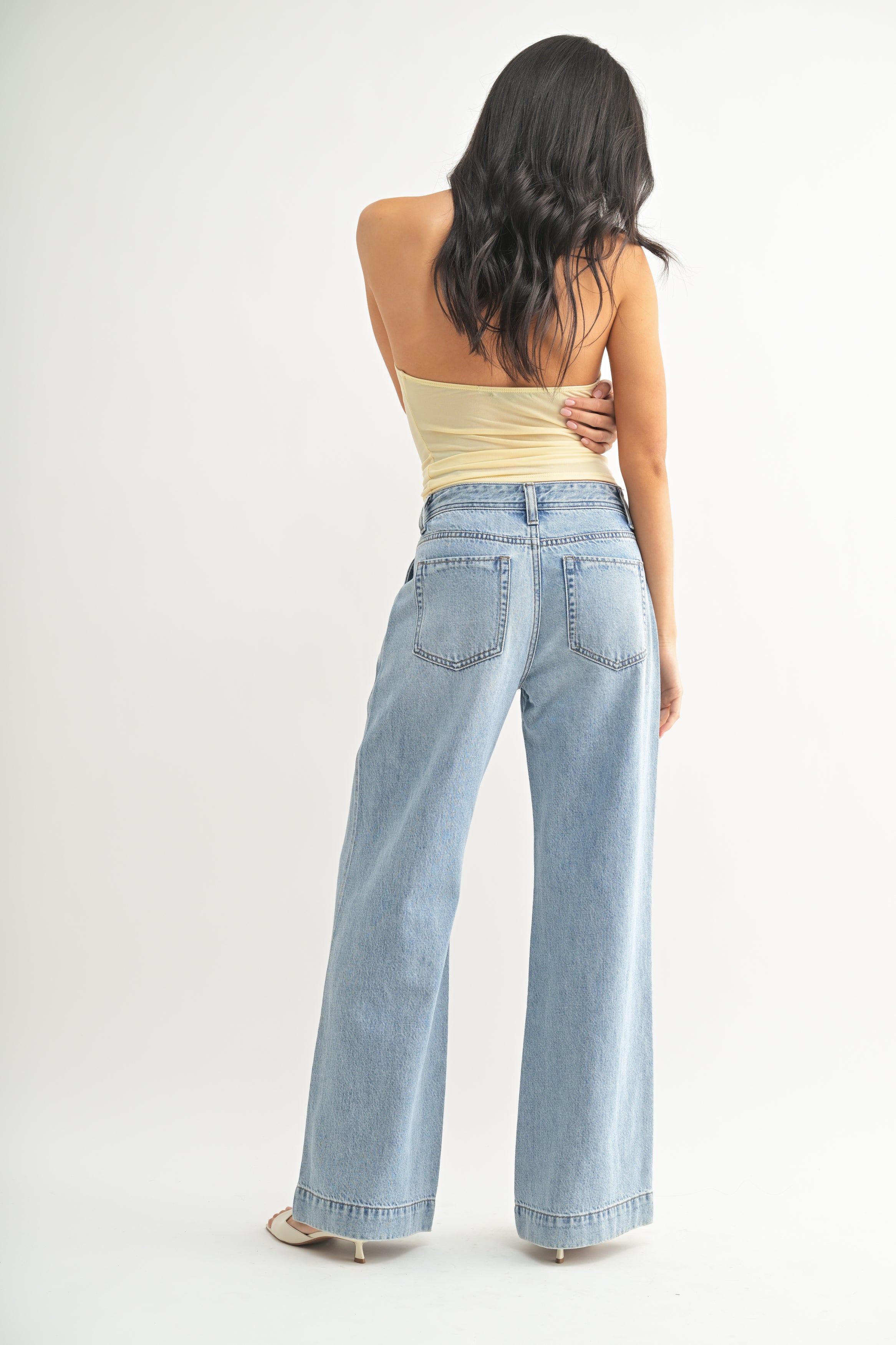 Woman wearing light blue jeans and a yellow top on a white background