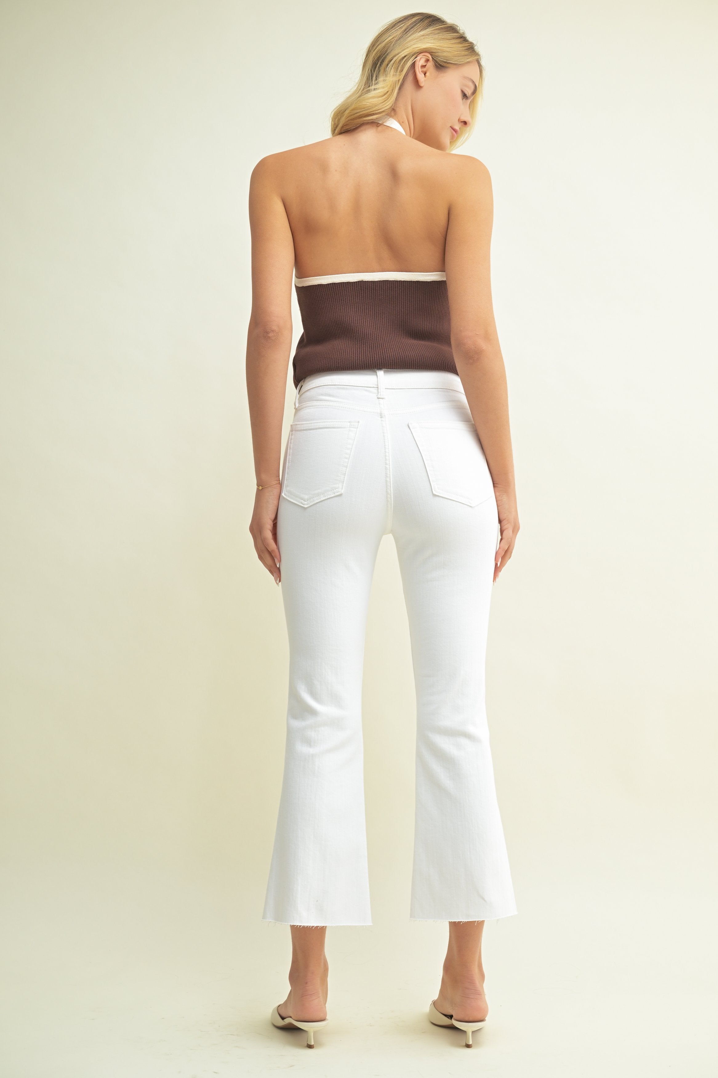 Woman wearing a brown top and white pants on a beige background