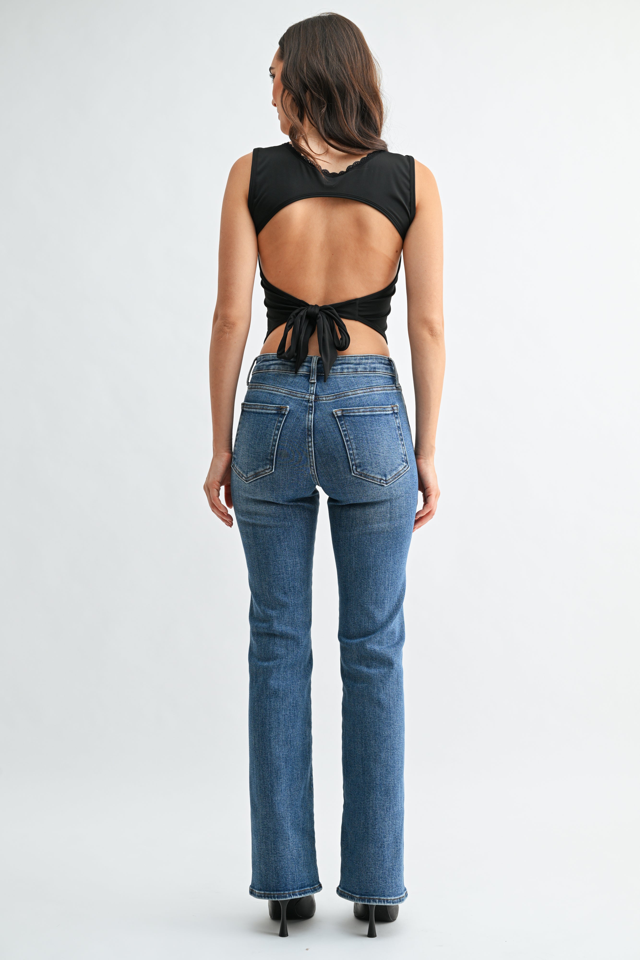 Woman wearing a black open-back top and blue jeans on a white background