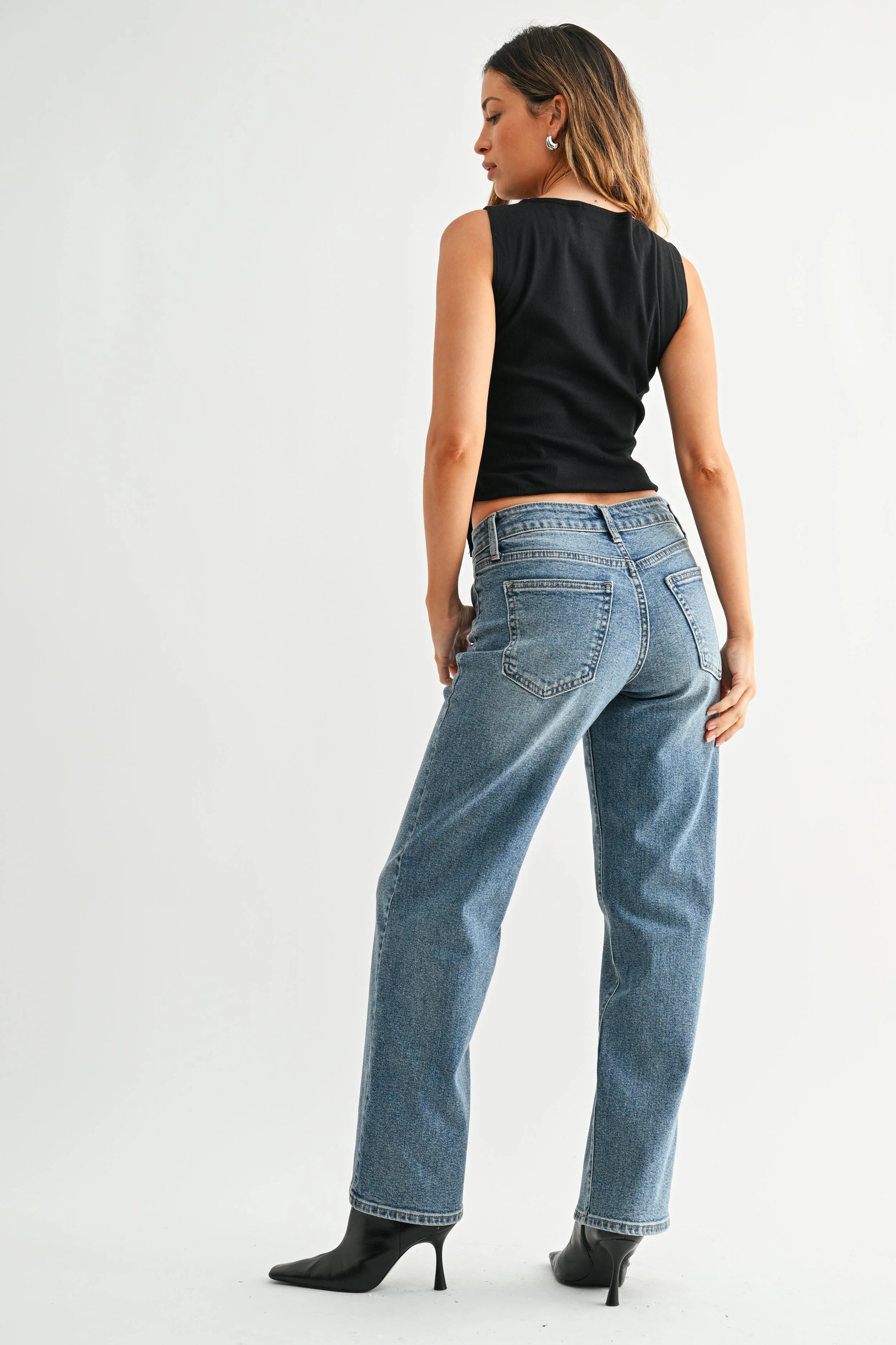 Woman wearing blue jeans and a black top on a white background