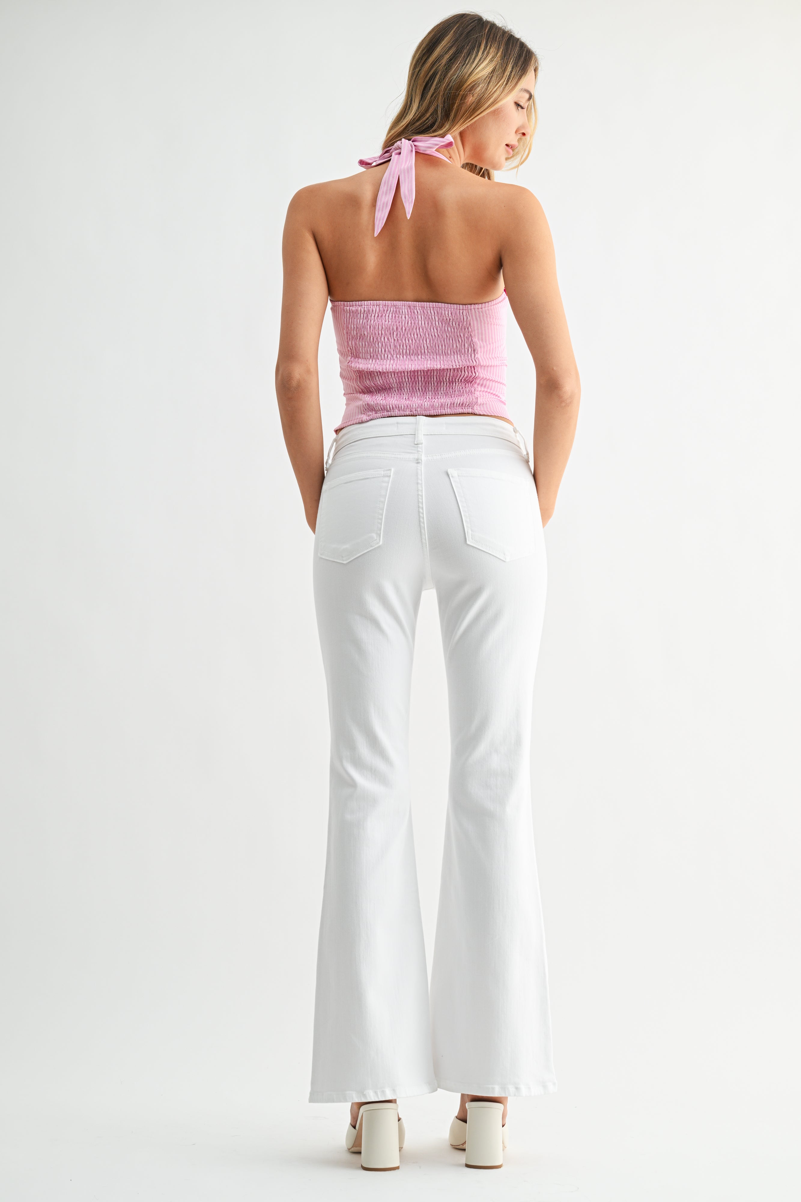 Woman wearing a pink strapless top and white pants on a white background