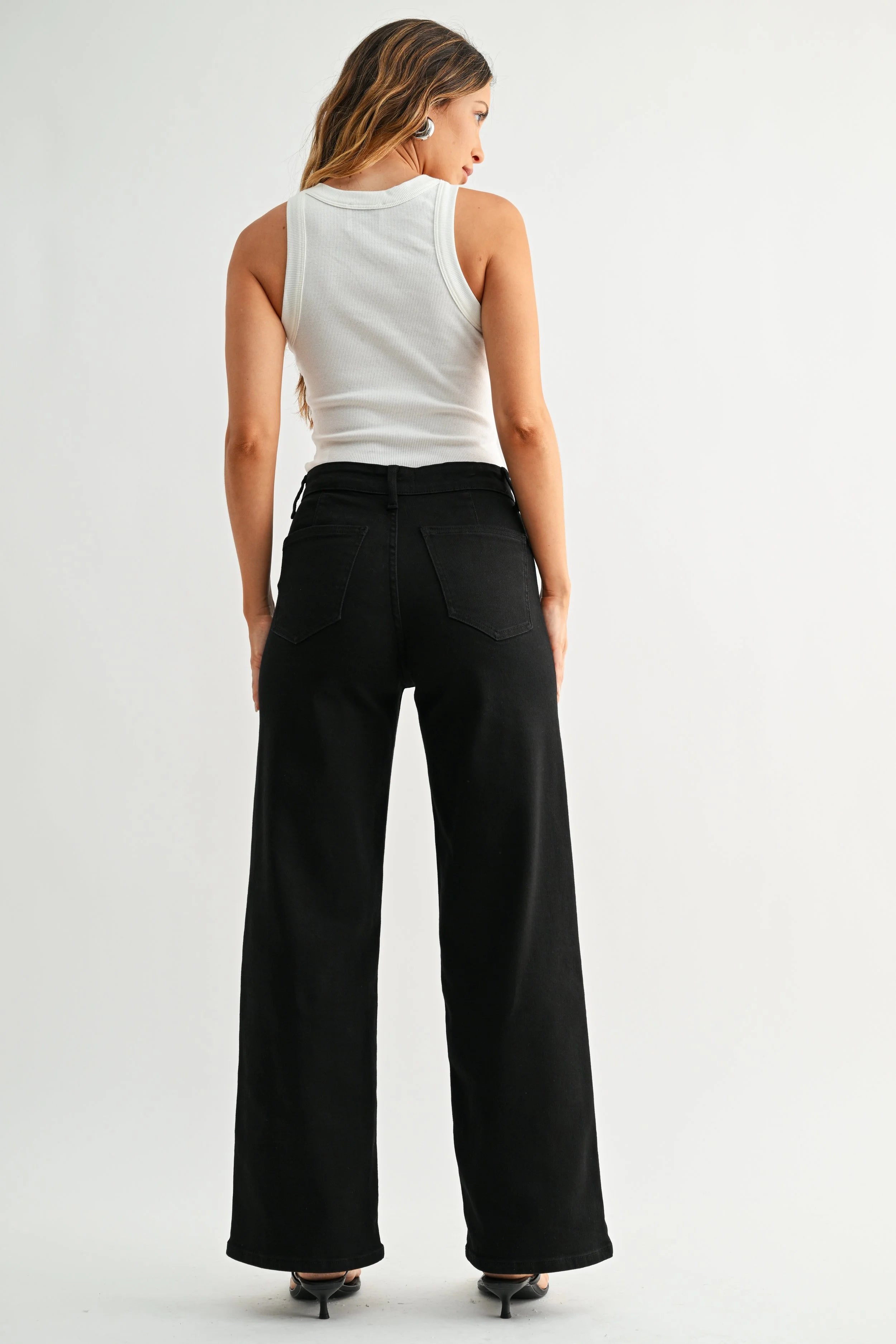 Person wearing a white sleeveless top and black wide-leg pants on a plain background