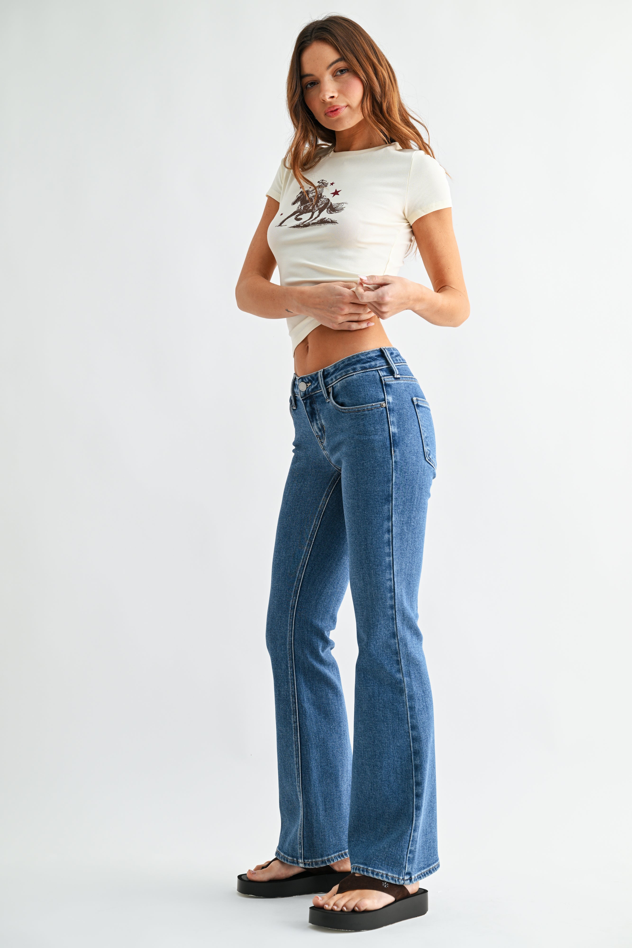 Woman wearing a white crop top with a graphic design and blue jeans on a white background