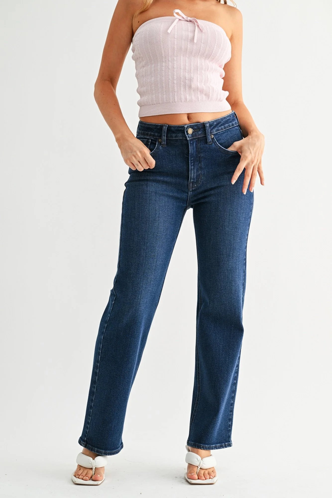 Woman wearing a white strapless top and blue jeans on a light gray background