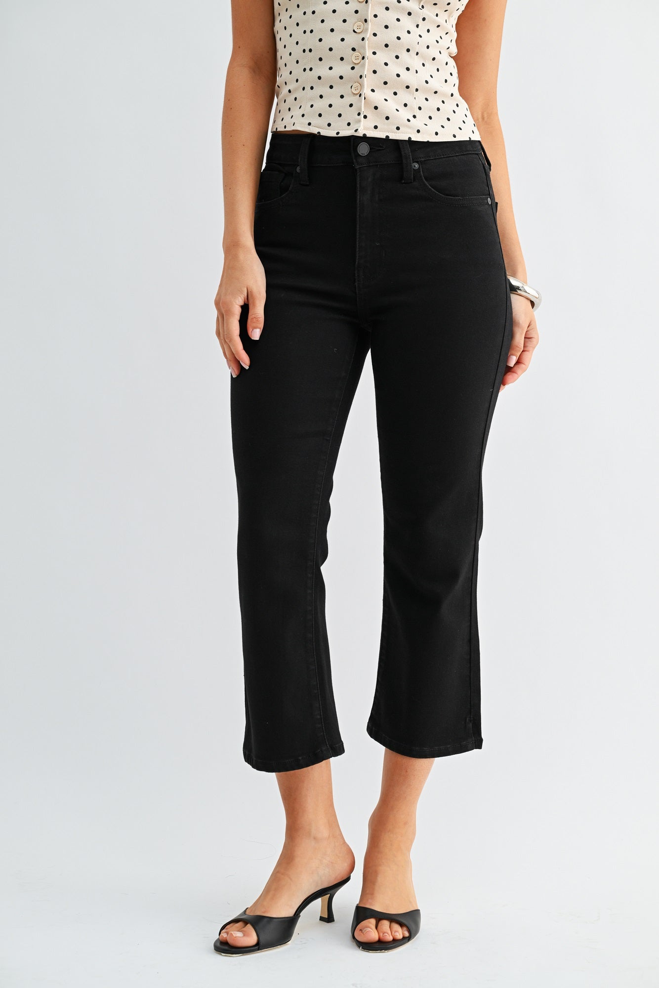Person wearing black jeans and a polka dot top on a light gray background