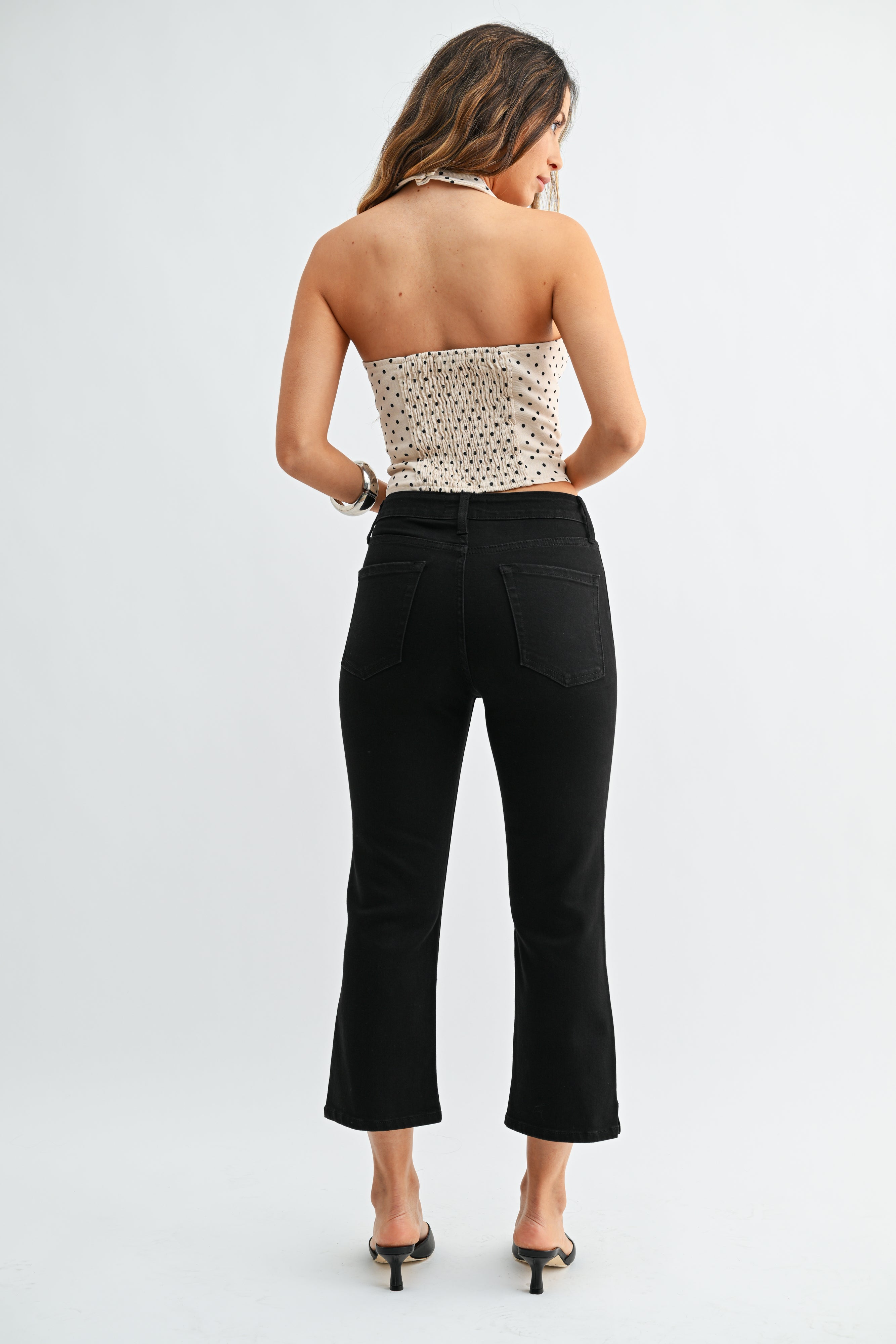 Woman wearing a strapless top with a polka dot pattern and black pants on a white background