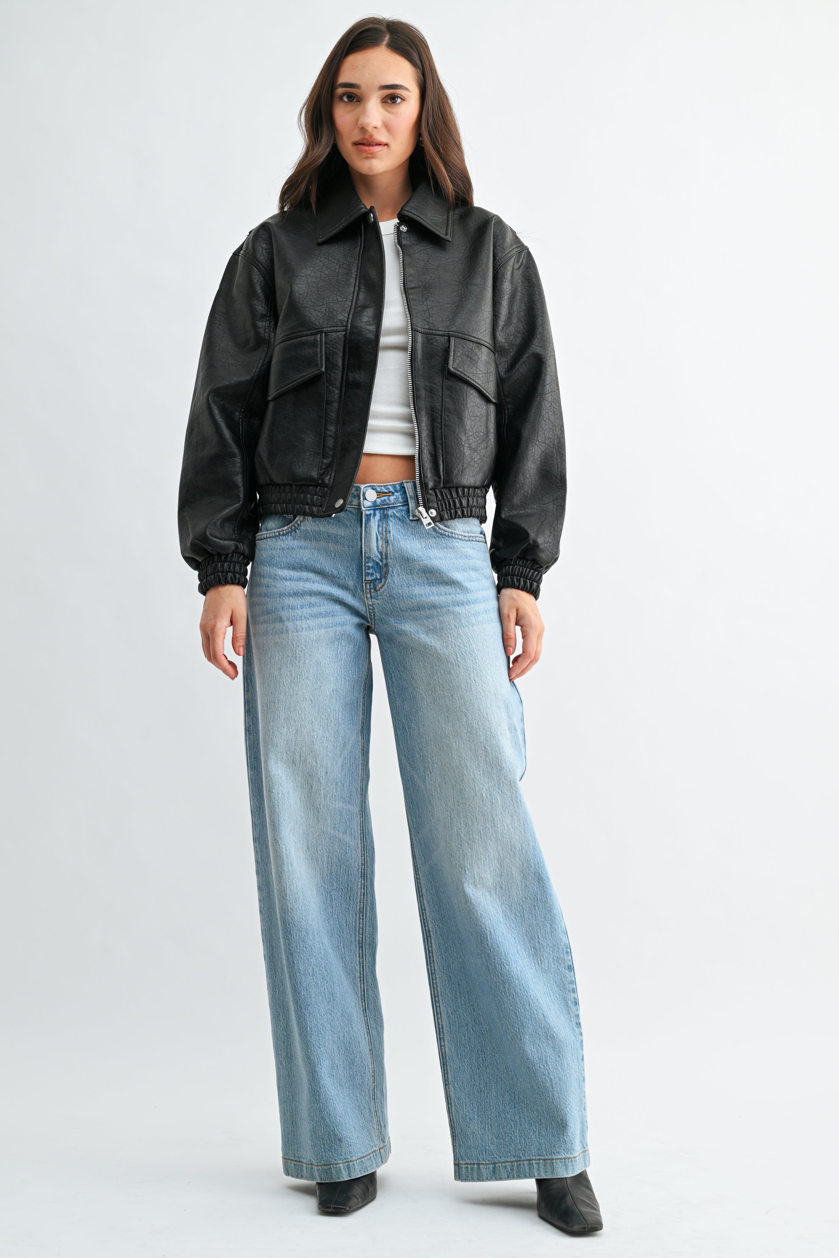 Person wearing a black leather jacket and light blue jeans on a white background