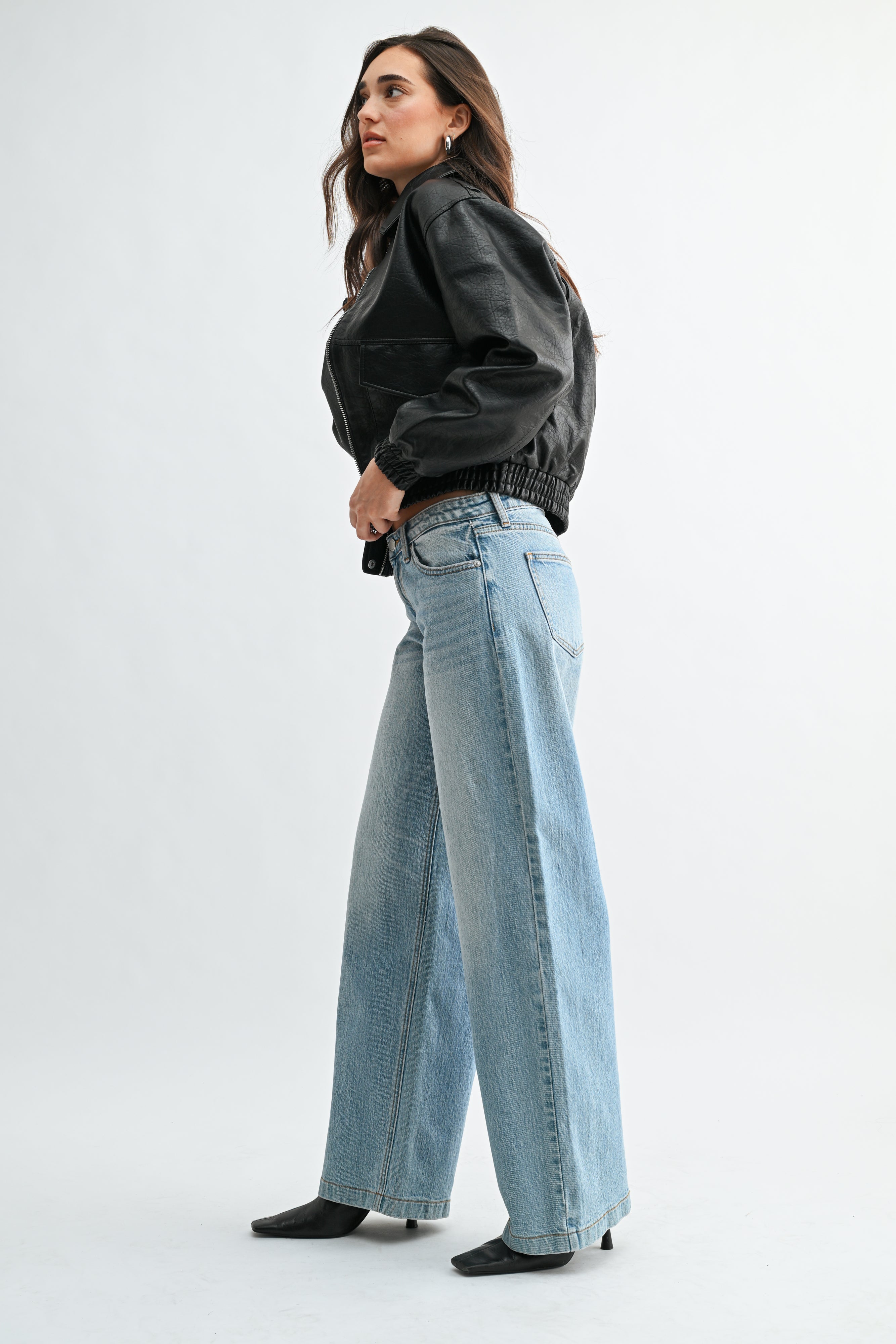 Woman wearing a black jacket and light blue jeans on a white background