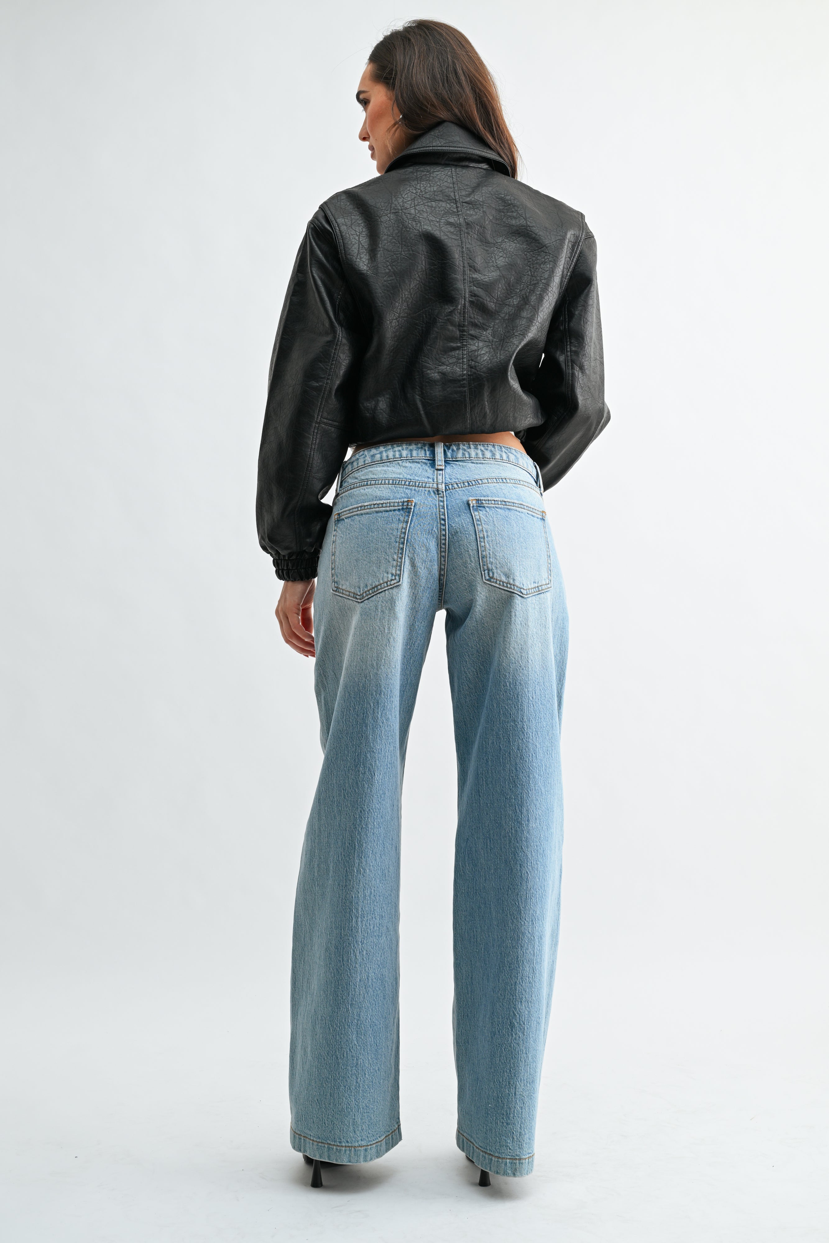 Person wearing a black leather jacket and light blue jeans on a white background