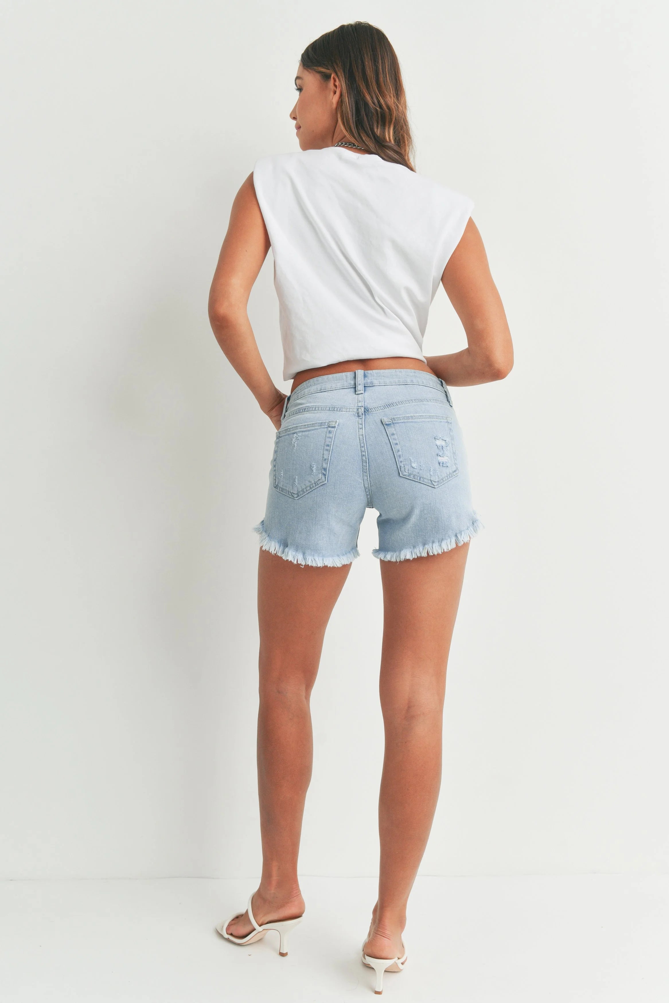 Woman wearing light blue denim shorts and a white top on a white background