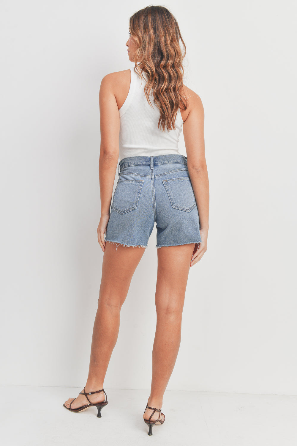 Woman wearing denim shorts and a white top on a plain background