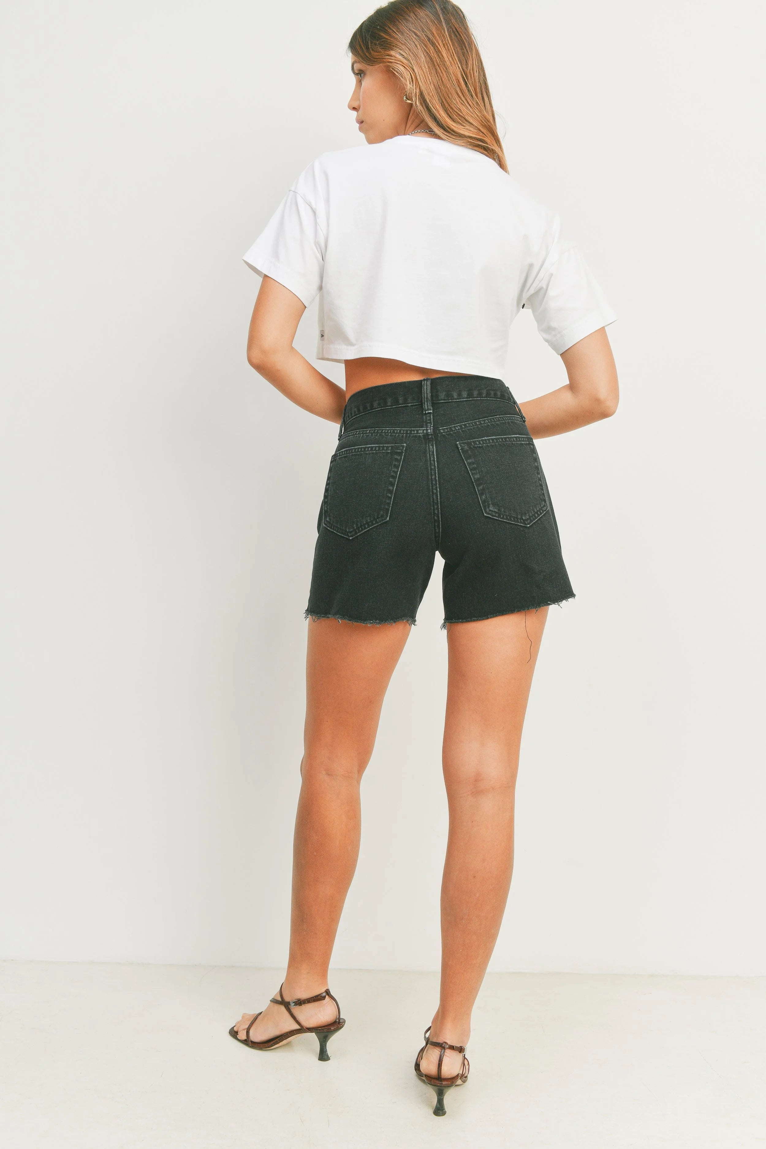 Person wearing black denim shorts and a white crop top on a plain background