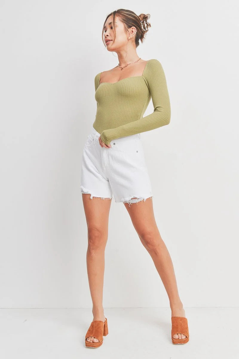 Woman wearing a green ribbed long-sleeve top and white shorts on a white background