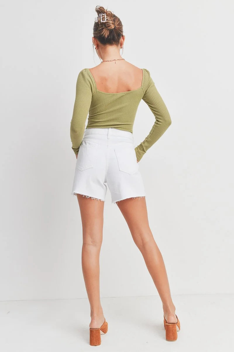 Person wearing a green long-sleeve top and white shorts on a plain background
