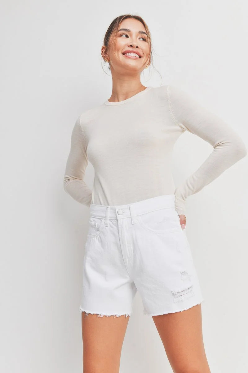 Woman wearing a white long-sleeve top and white shorts on a plain background