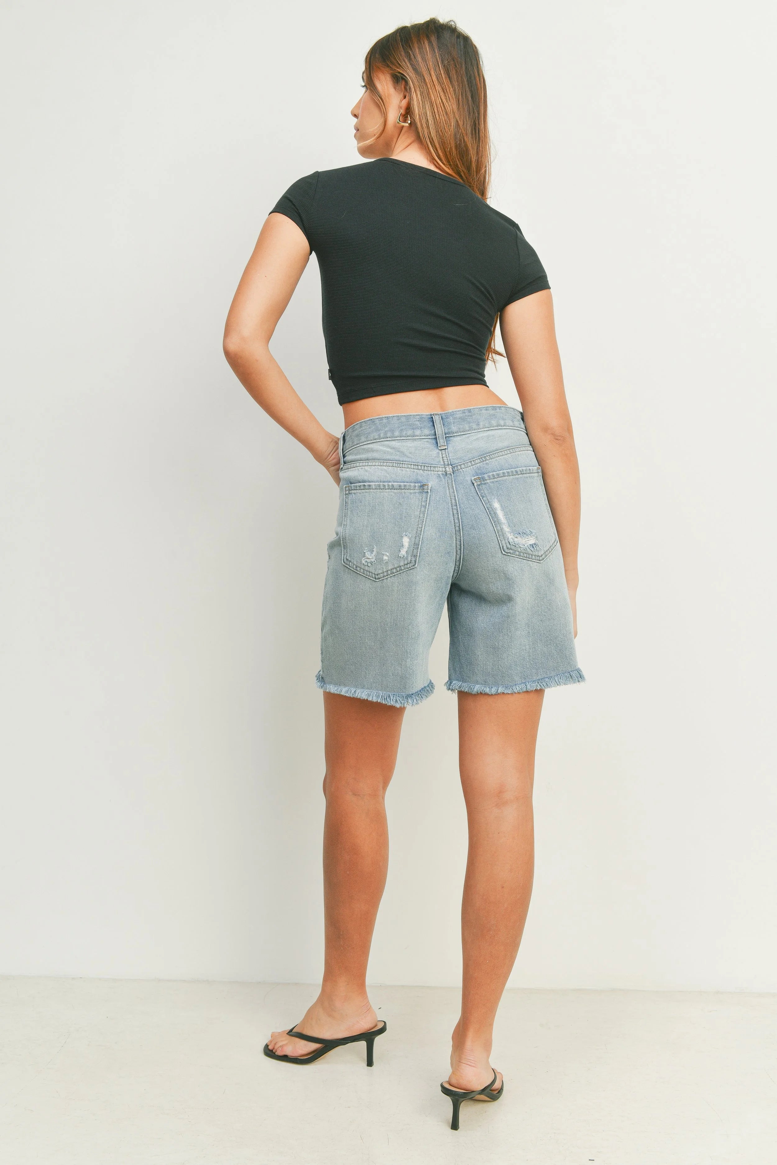 Woman wearing a black crop top and denim shorts on a white background