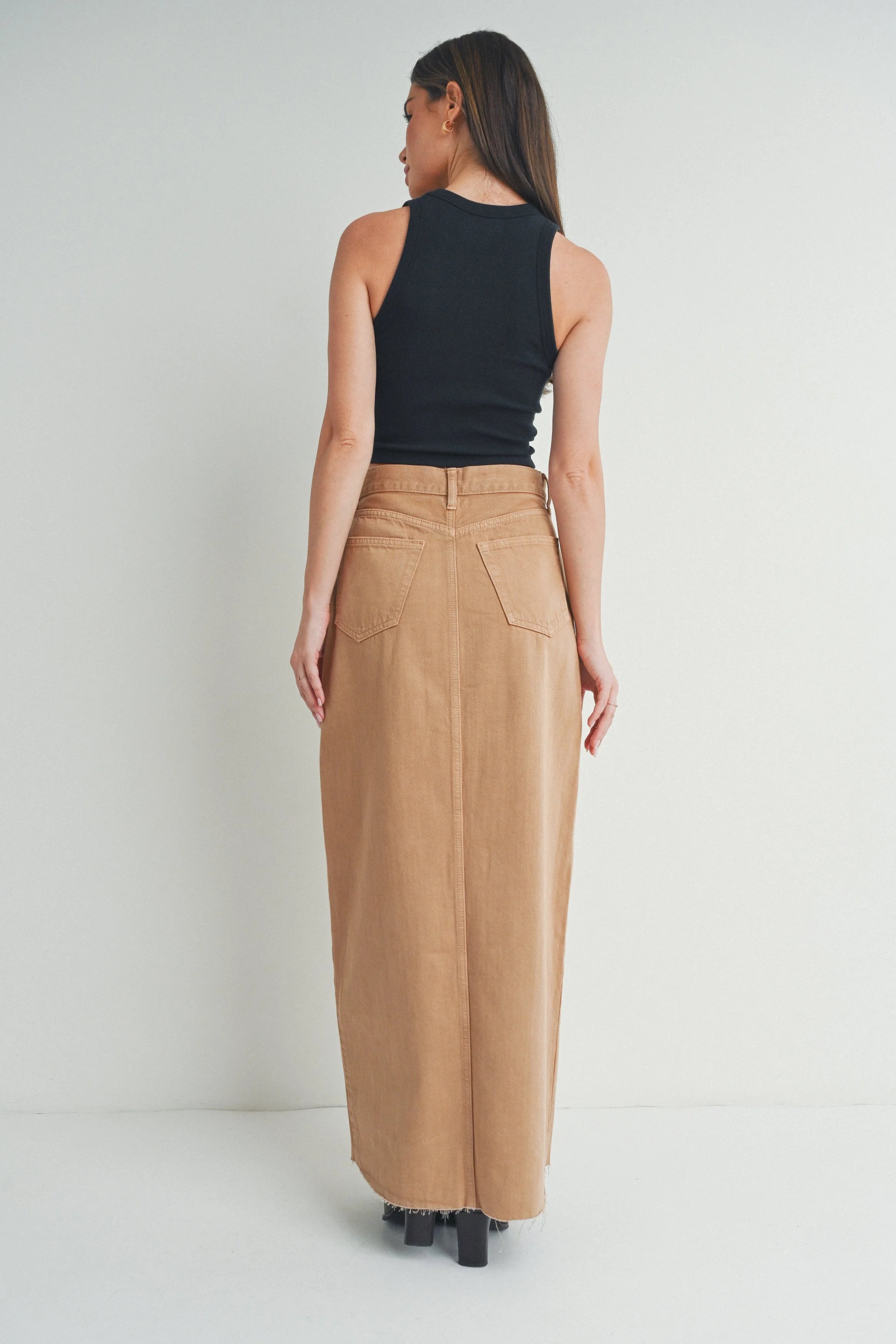 Woman wearing a black sleeveless top and tan long skirt on a white background