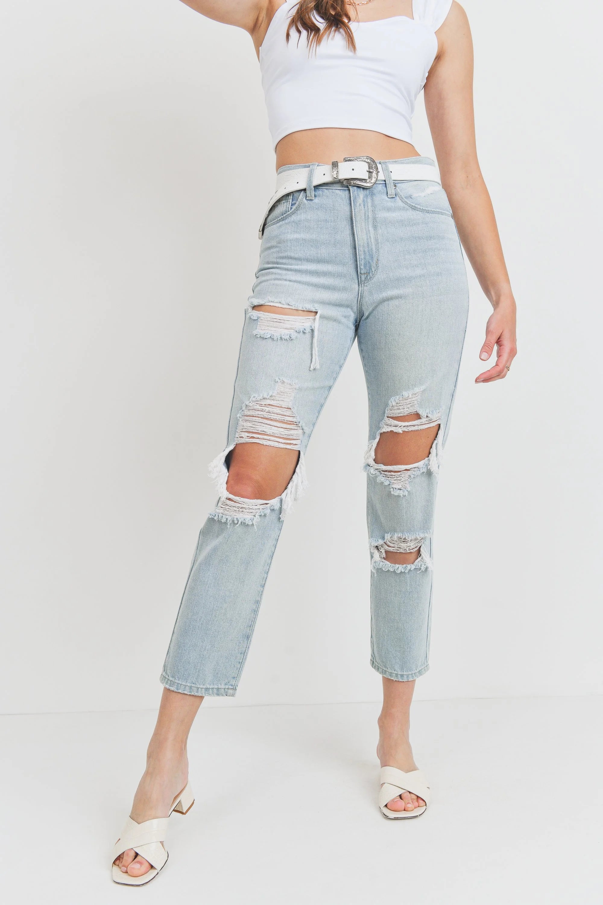 Person wearing light blue ripped jeans and a white top on a plain background