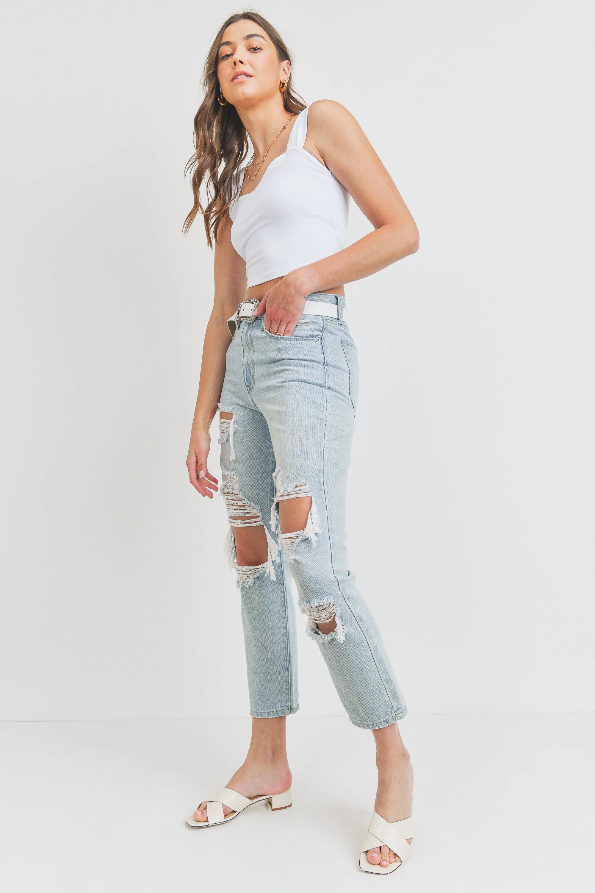 Woman wearing a white top and light blue ripped jeans on a white background