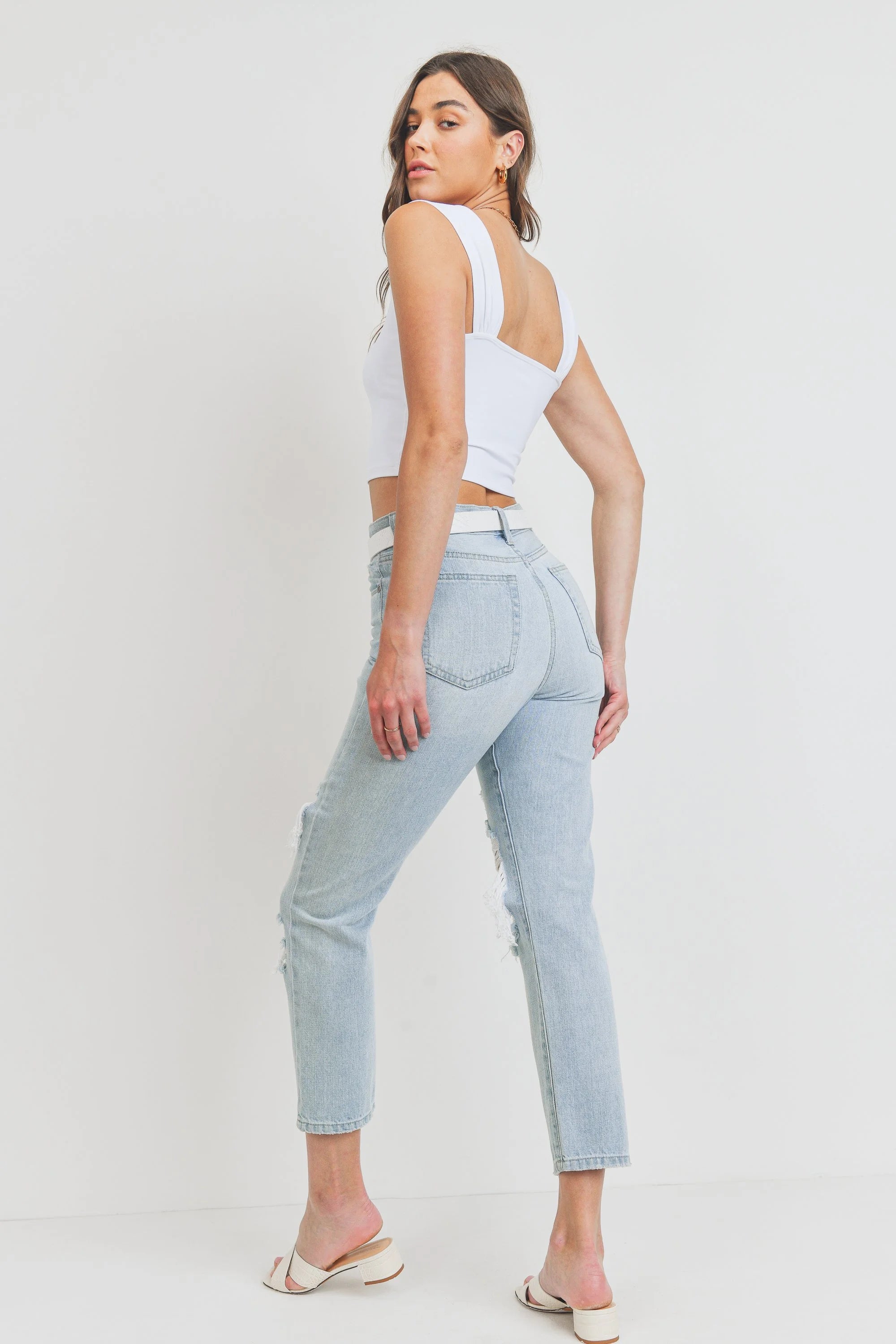 Woman wearing light blue jeans and a white top on a plain background