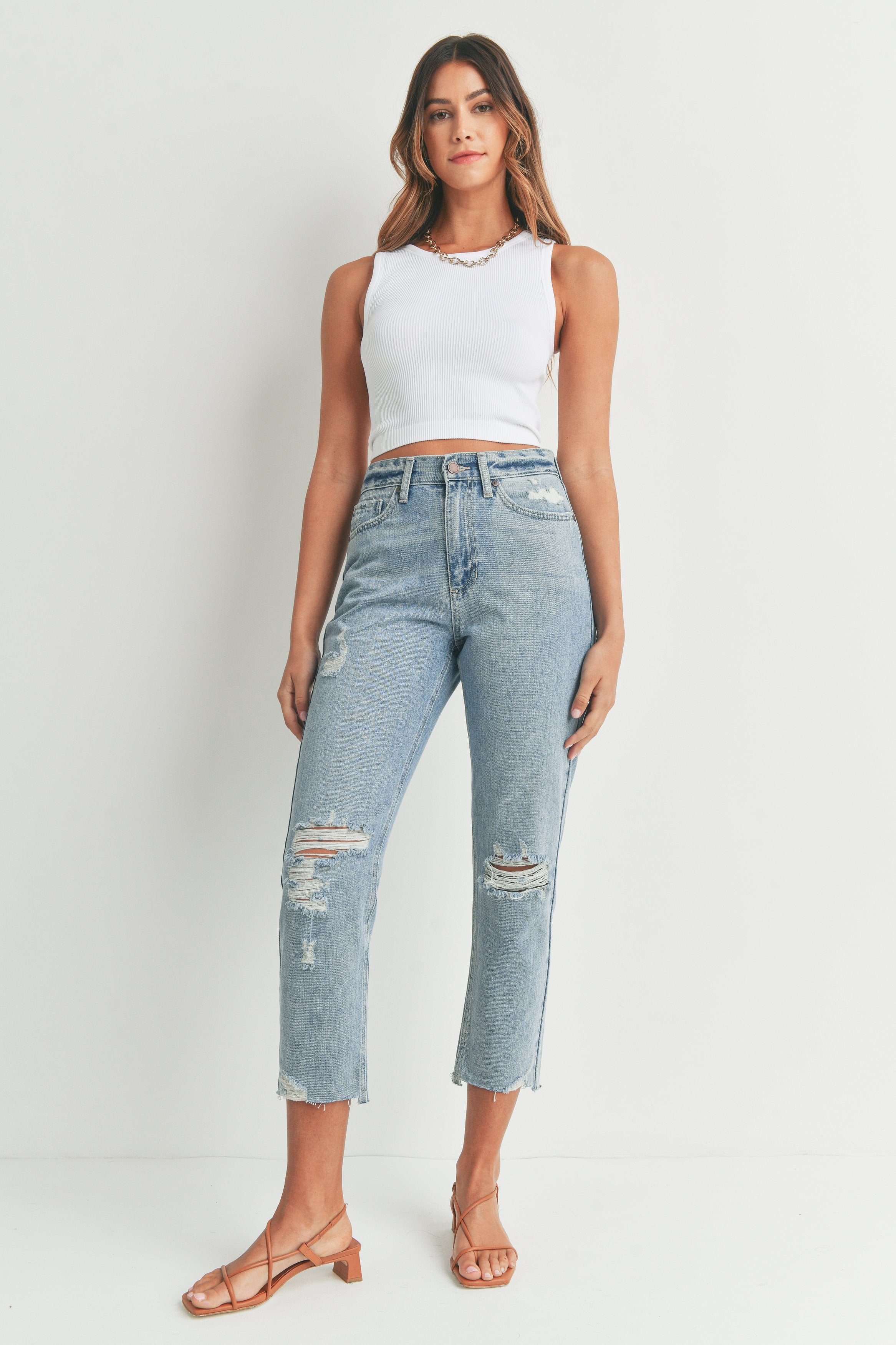 Woman wearing a white sleeveless top and distressed jeans on a plain background