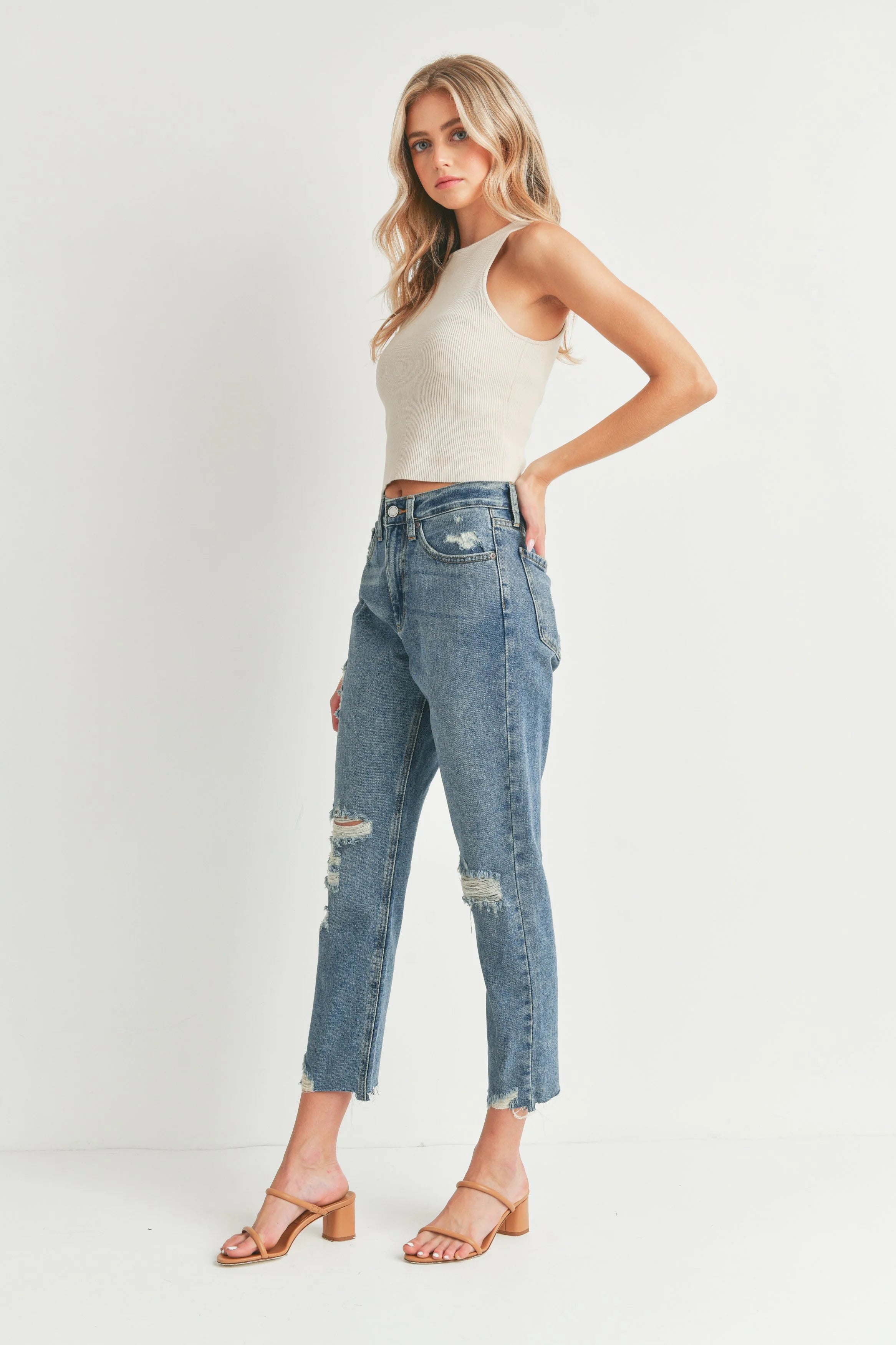 Woman wearing a white tank top and blue jeans on a plain background