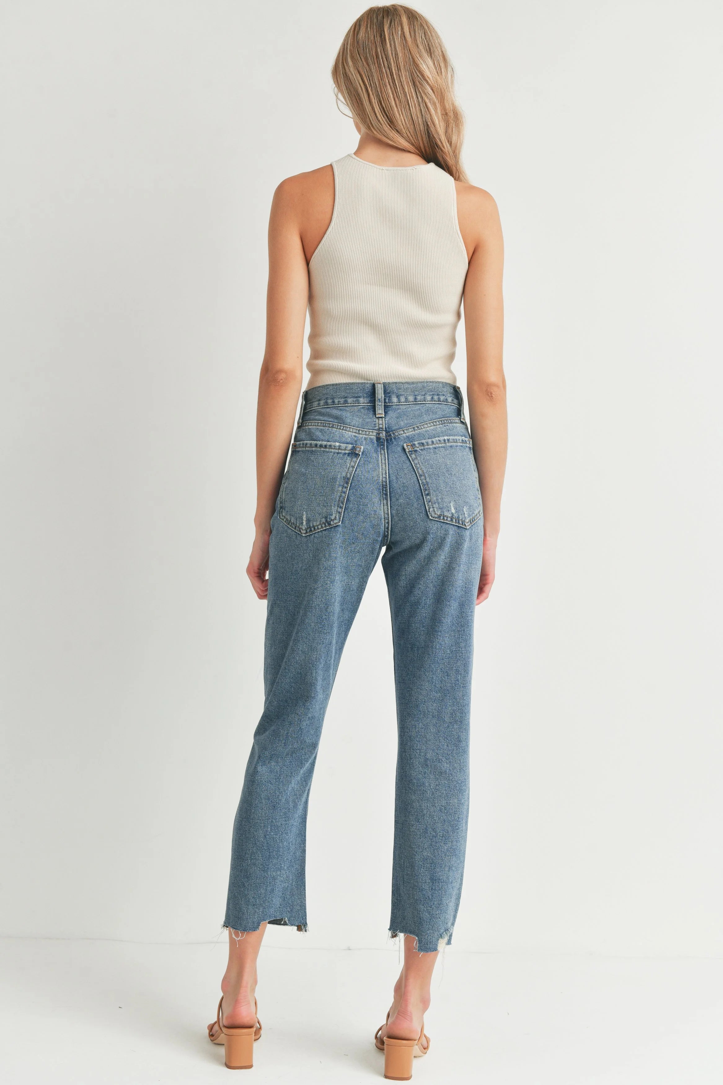 Woman wearing blue jeans and a white top on a light gray background