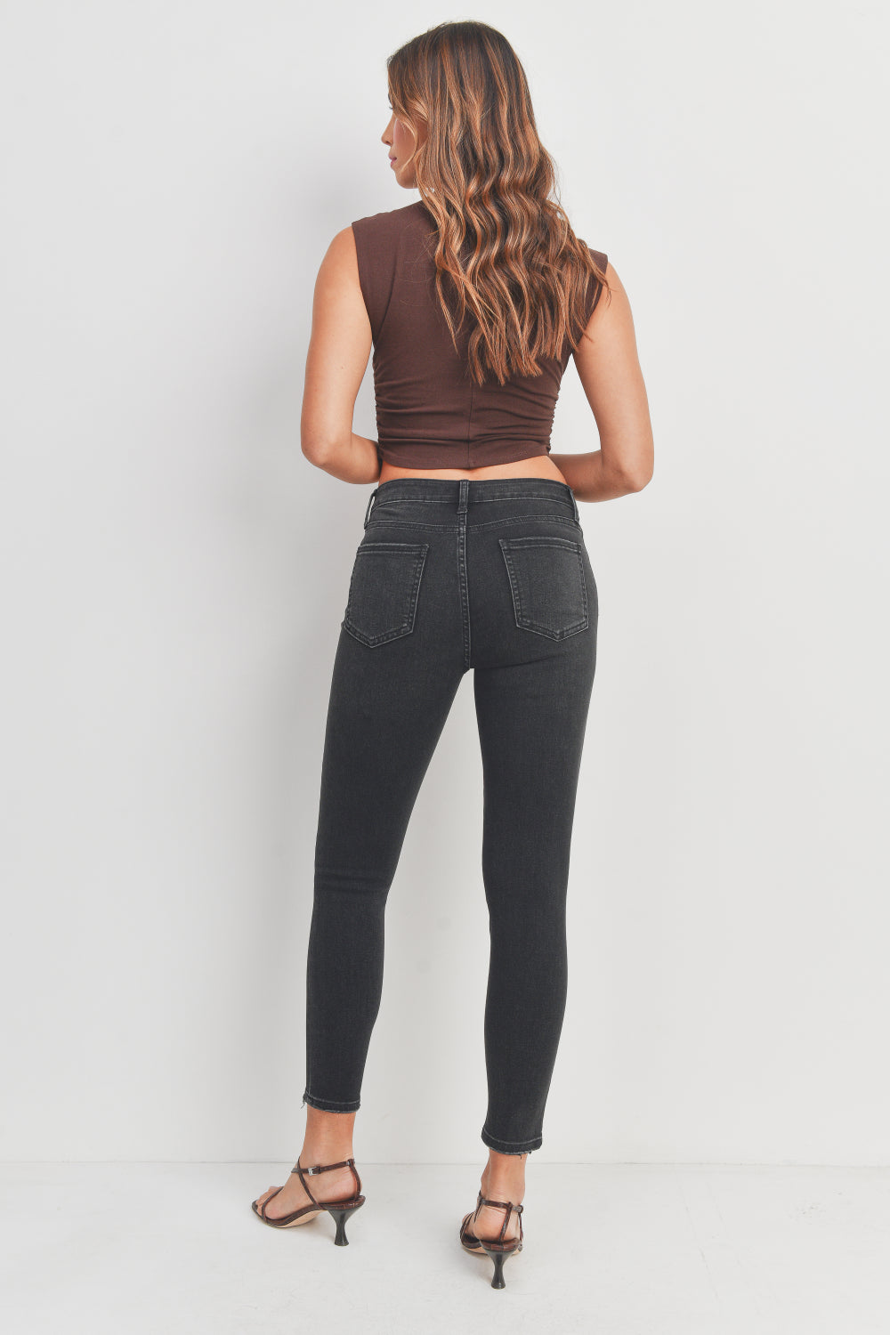 Woman wearing black jeans and a brown top on a white background