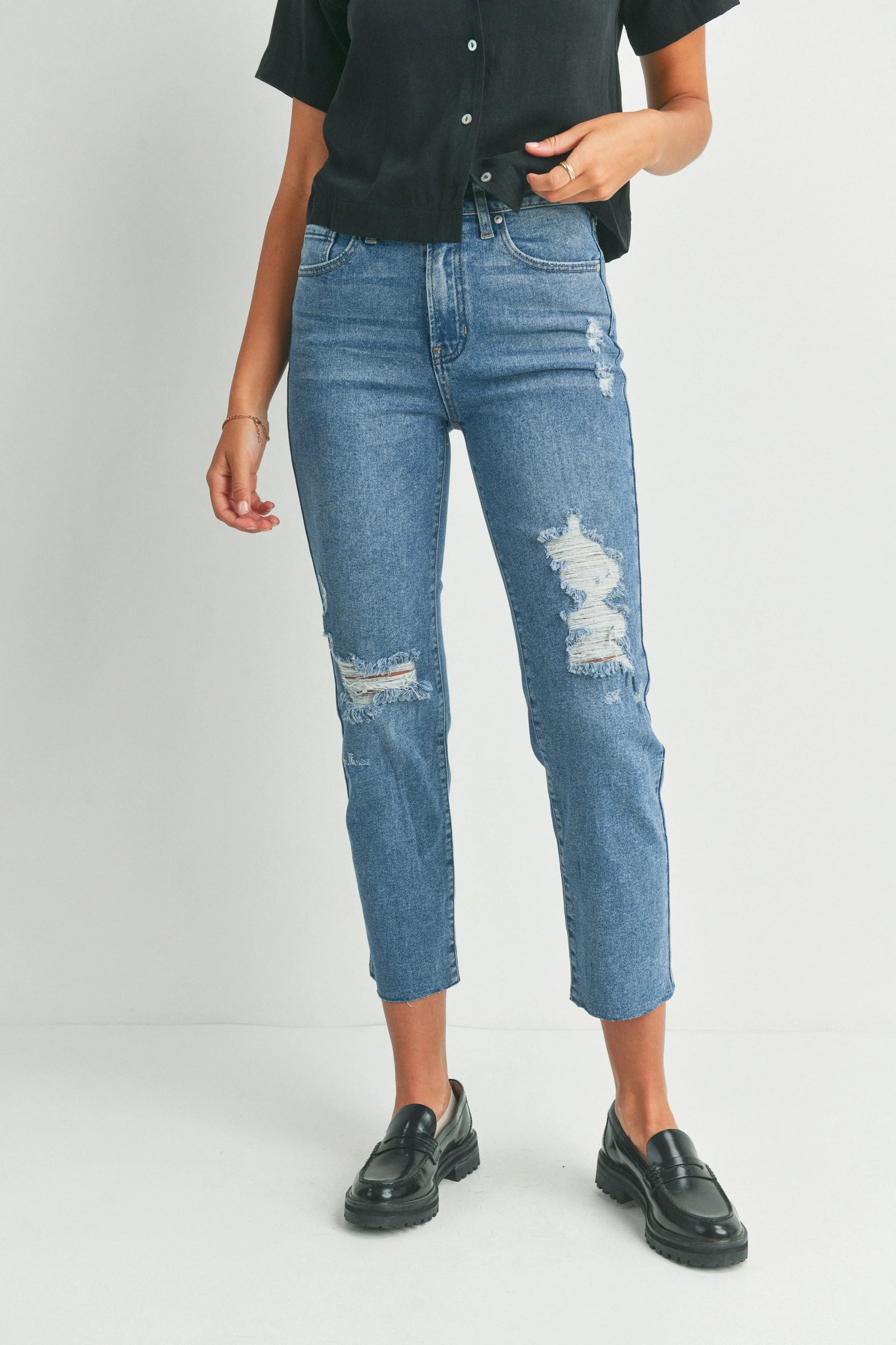 Person wearing blue distressed jeans and black shoes on a plain background